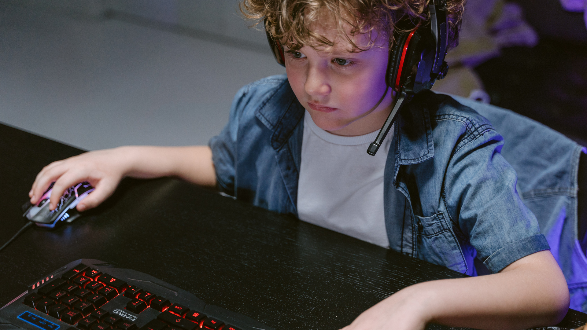 A child wearing a gaming headset plays a videogame on a PC.