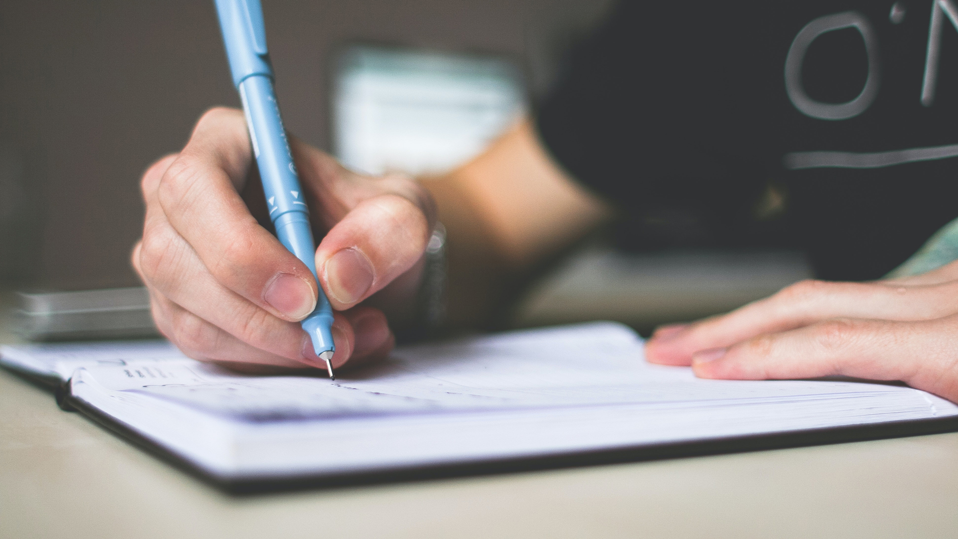 A person making a list in a notebook with a blue pen.