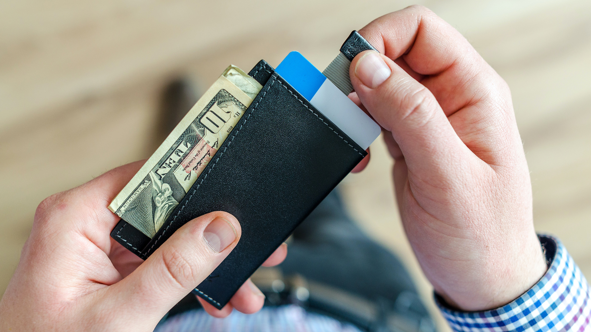 A person pulls out a wallet with a ten dollar bill and credit cards hanging out.