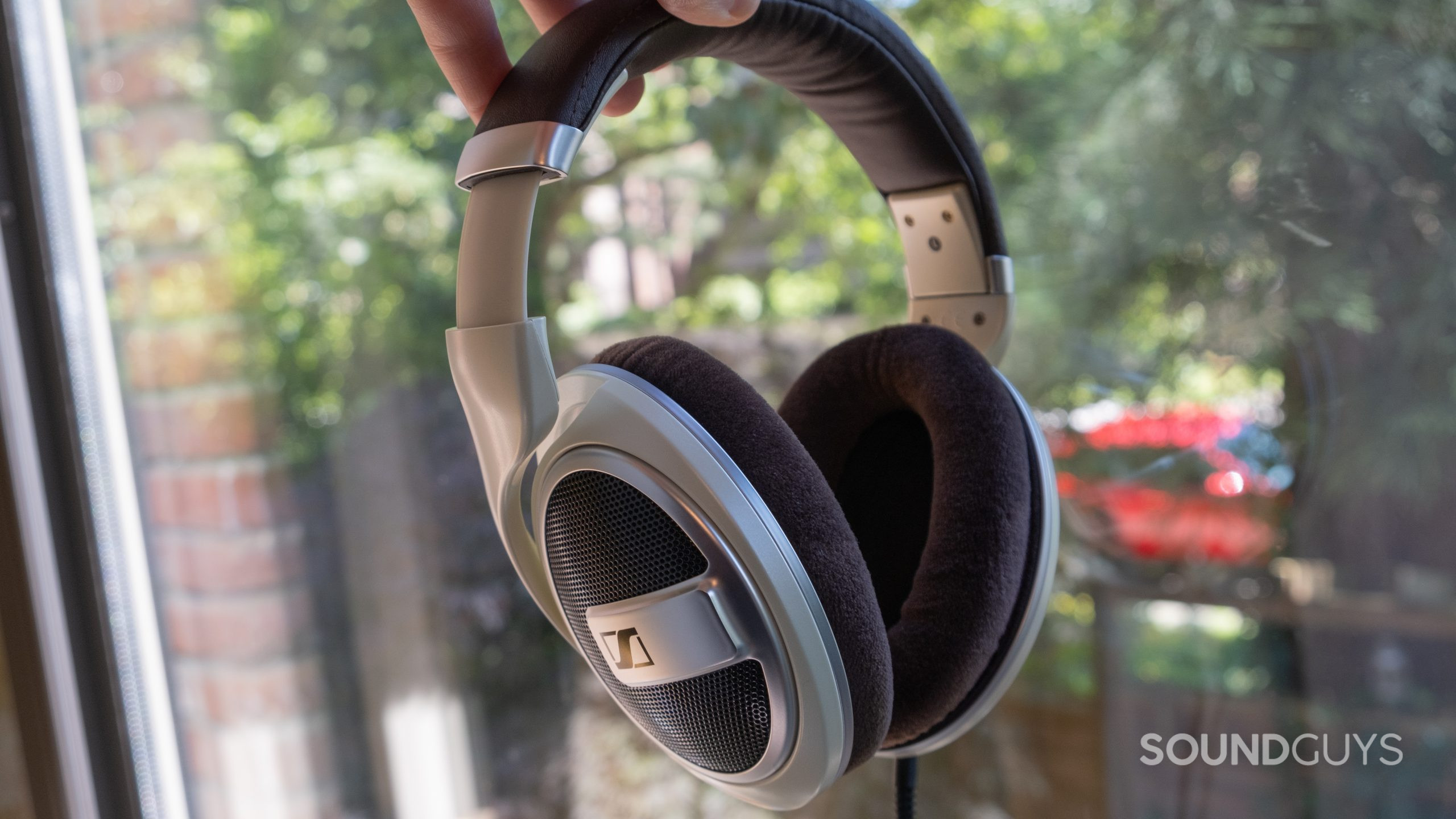 A hand holds the Sennheiser HD 599 in front of a window with greenery.