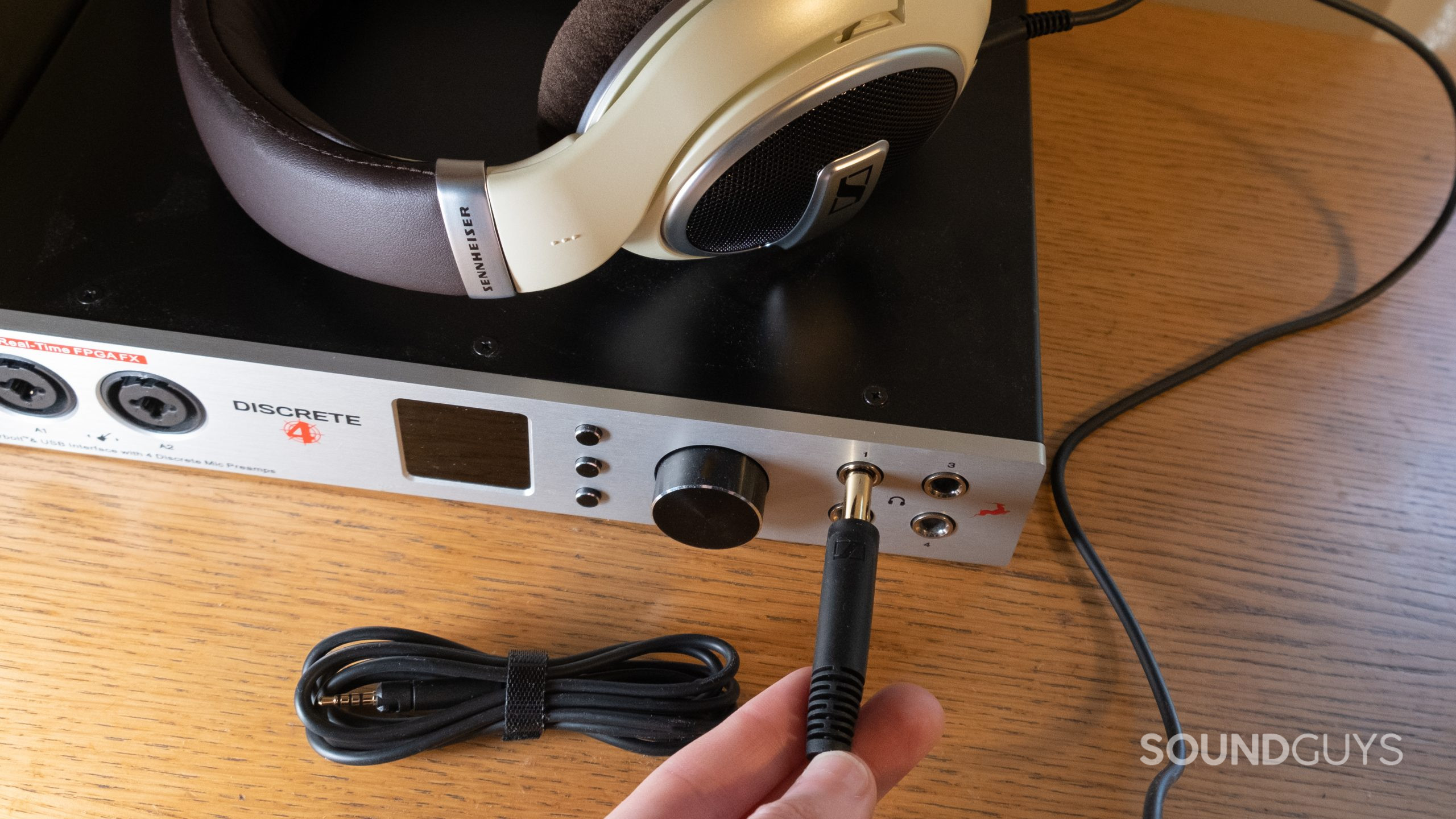 The Sennheiser HD 599 rests on top of an audio interface with the 1/4-inch cable held in a hand inserting it into the headphone output. A wrapped 3.5mm cable rests nearby.