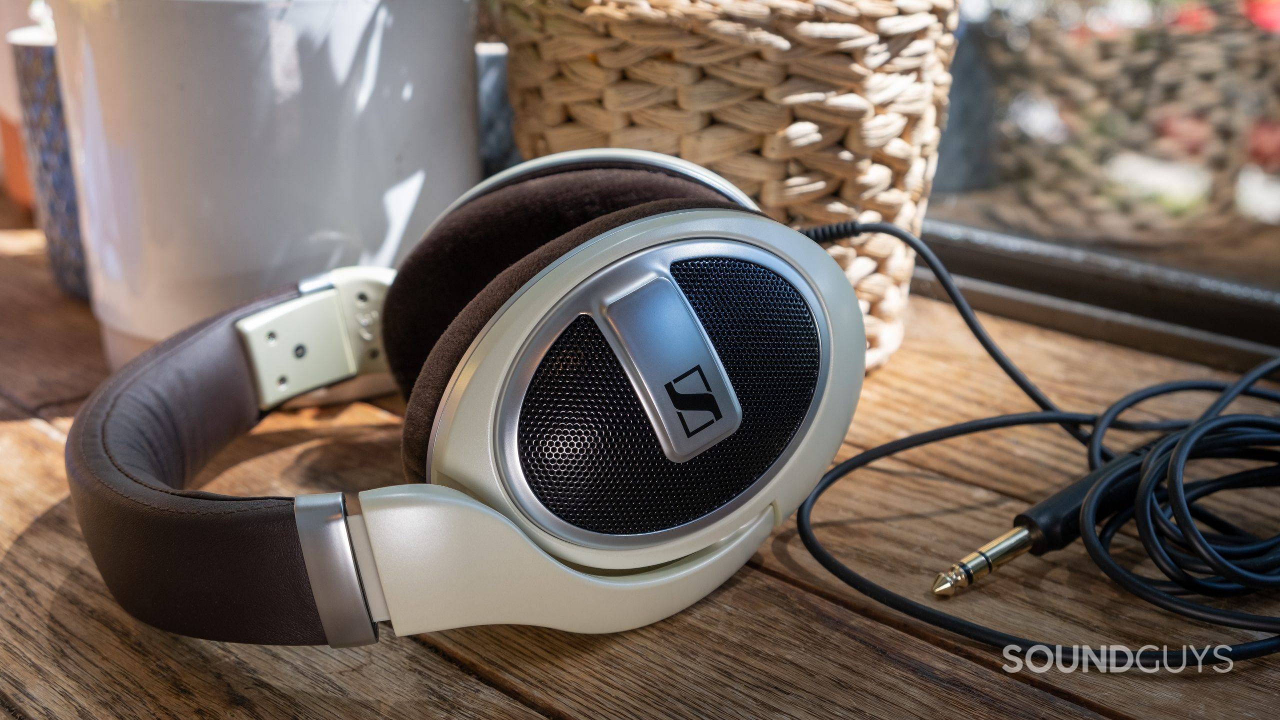 On a wood surface the Sennheiser HD 599 lays on its side showing the cable with pots and window in the background.
