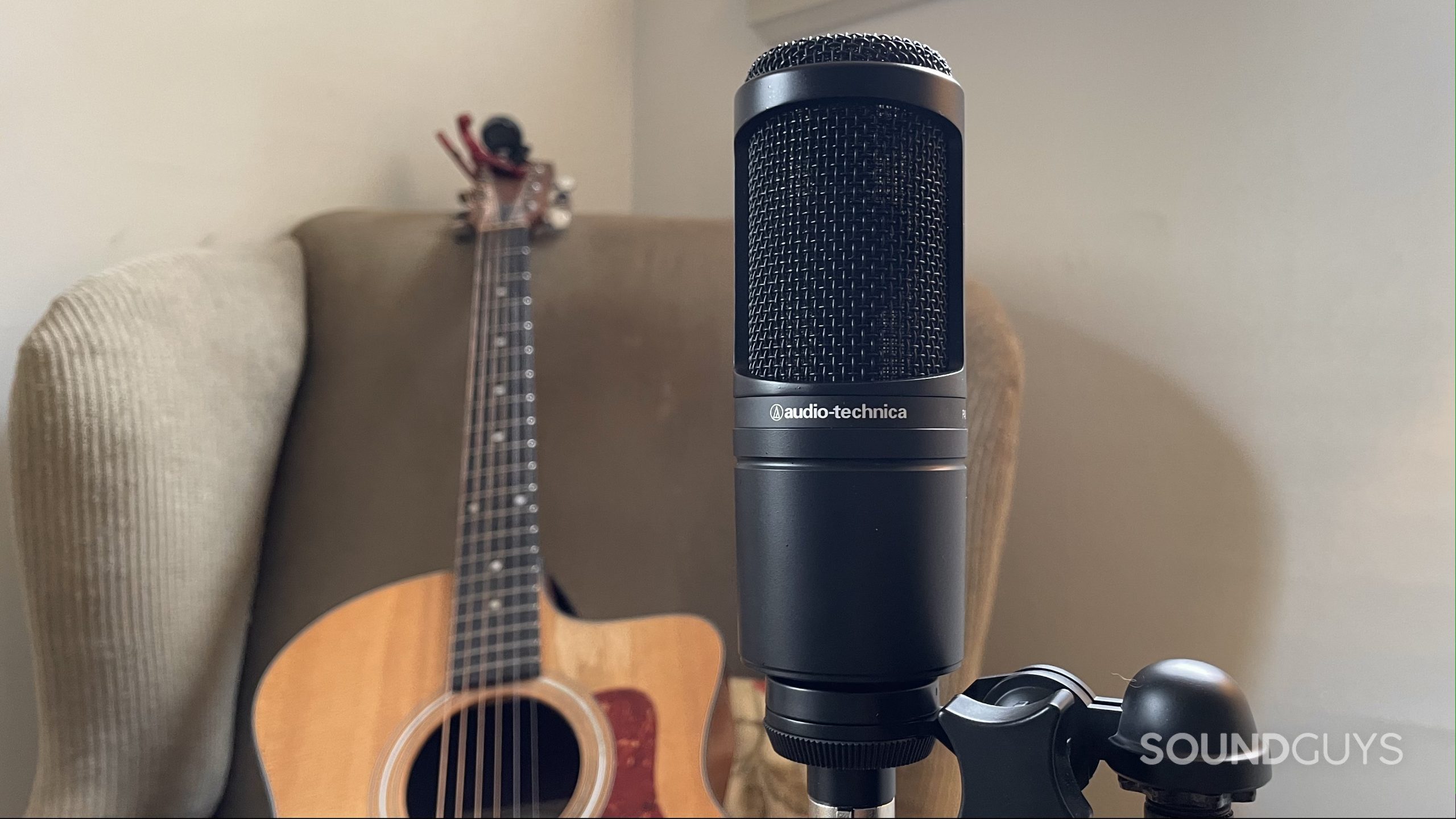 Audio-Technica AT2020 with an acoustic guitar resting on an armchair in the background.