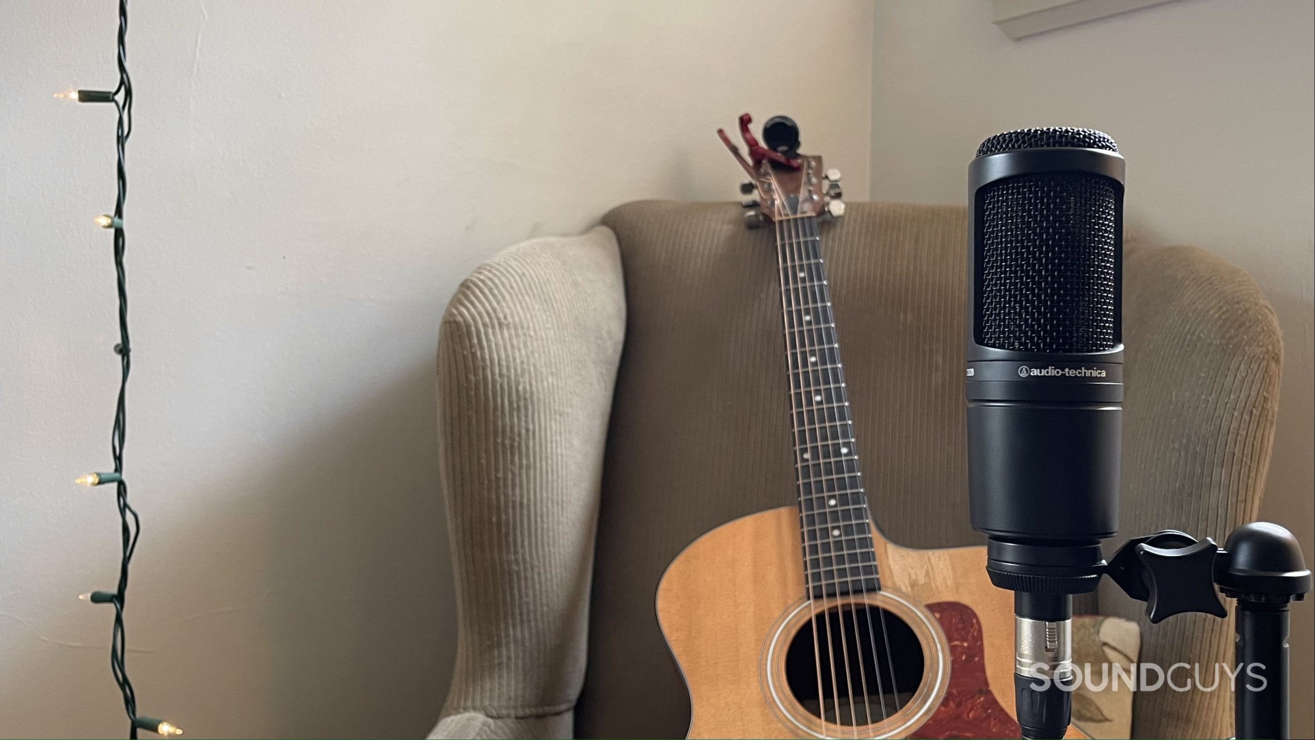 Audio-Technica AT2020 with a string of lights and acoustic guitar resting on an armchair in the background.