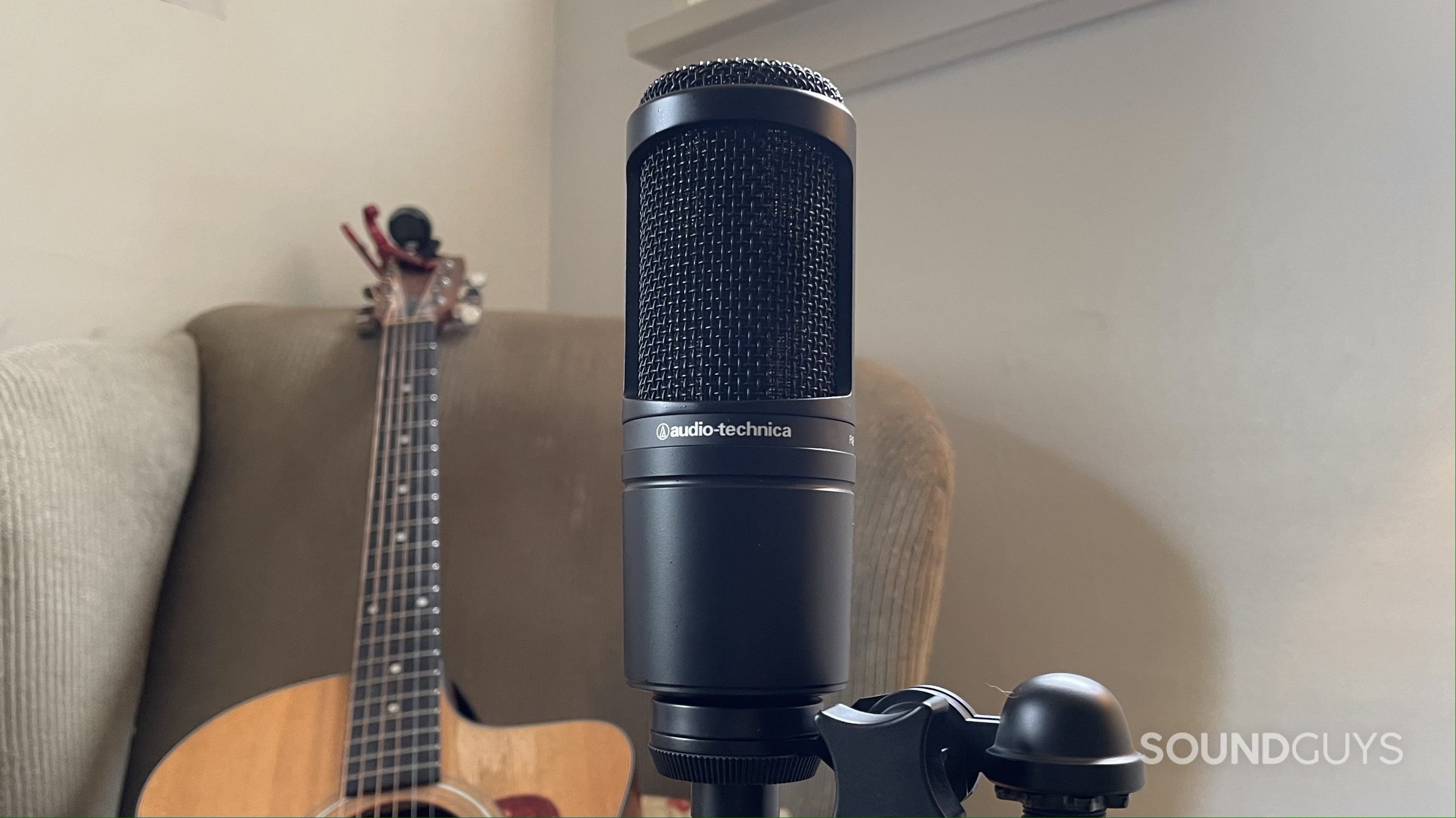 Audio-Technica AT2020 with an acoustic guitar resting on an armchair in the background.