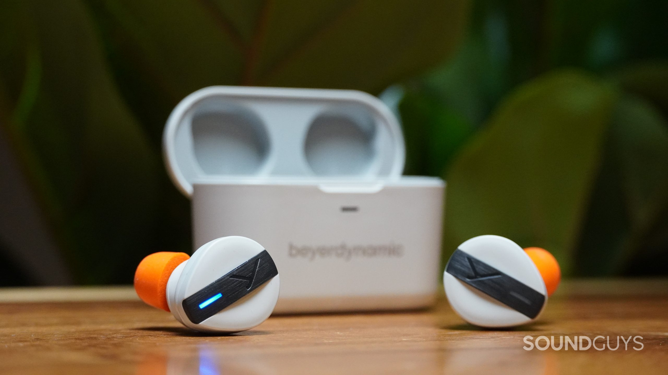 Beyerdynamic Free BYRD earbuds in front of charging case on a wood table.