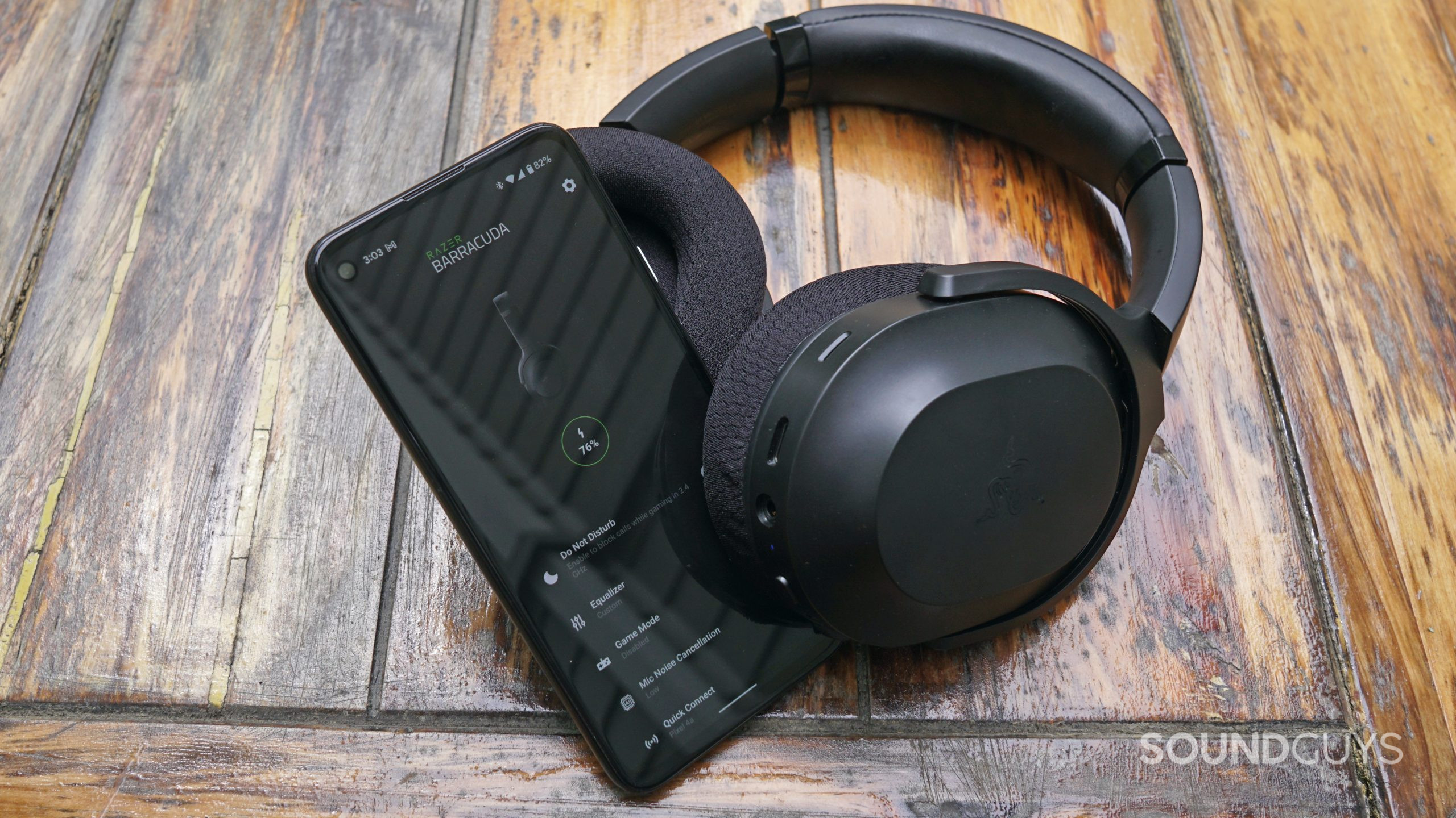 The Razer Barracuda lays on a wooden table next to a Google Pixel 4a running the Razer Audio app.