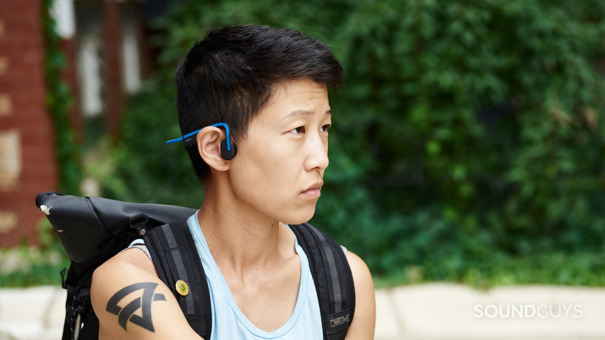 A person wears the Shokz OpenMove bone conduction headphones in blue while they sit outside.