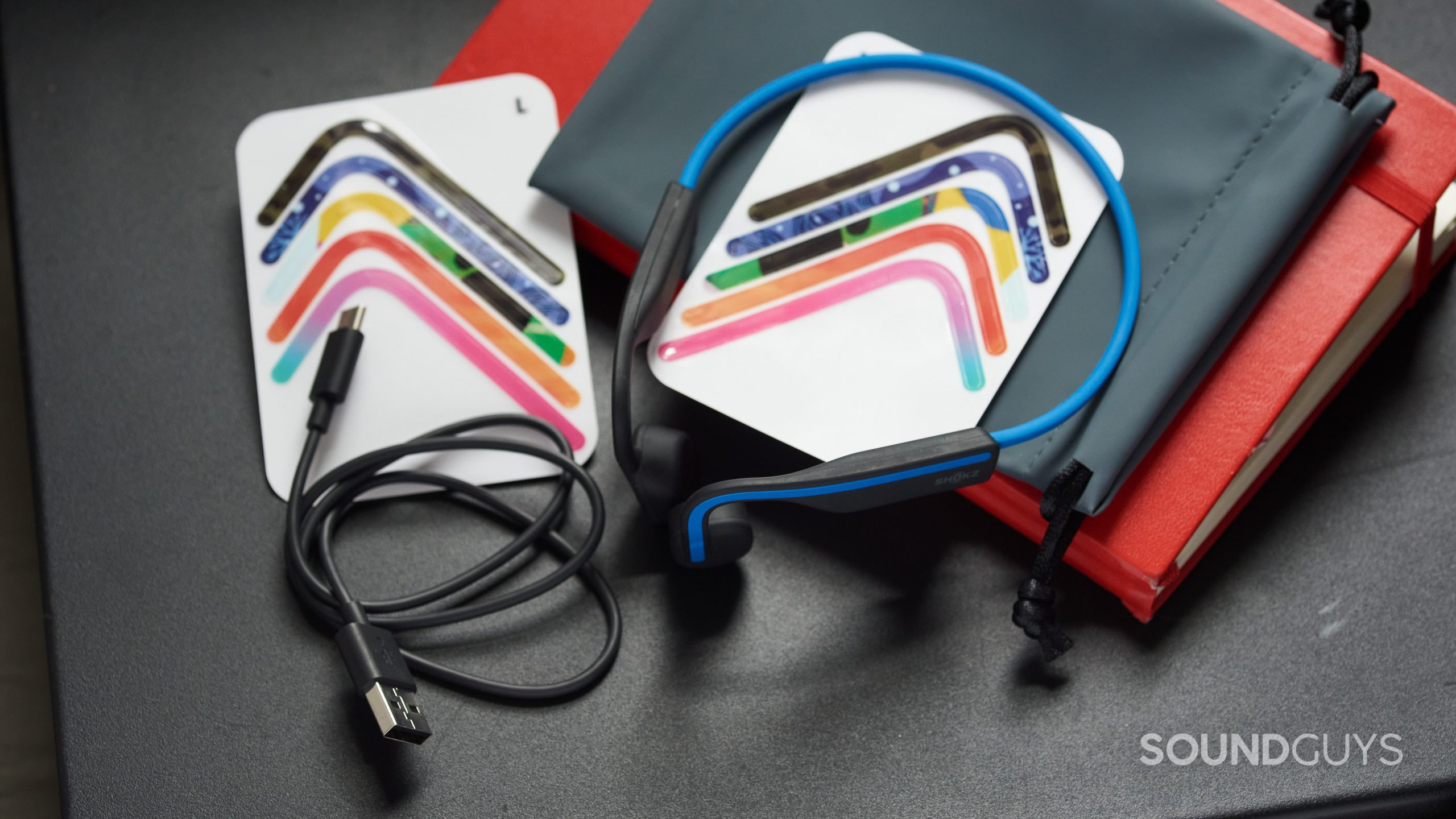 The Shokz OpenMove bone conduction headphones and all of the accessories, including stickers, a USB-C charging cable, and a drawstring pouch.