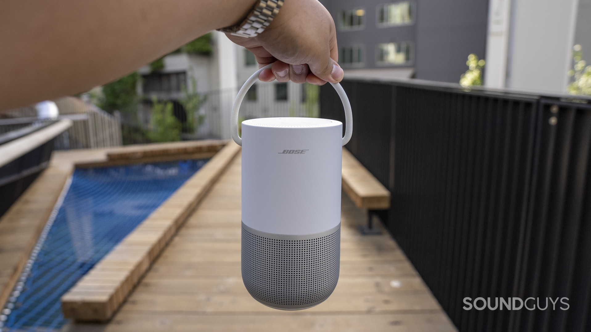 A hand holding a Bose Portable Smart Speaker by its built-in carrying handle.