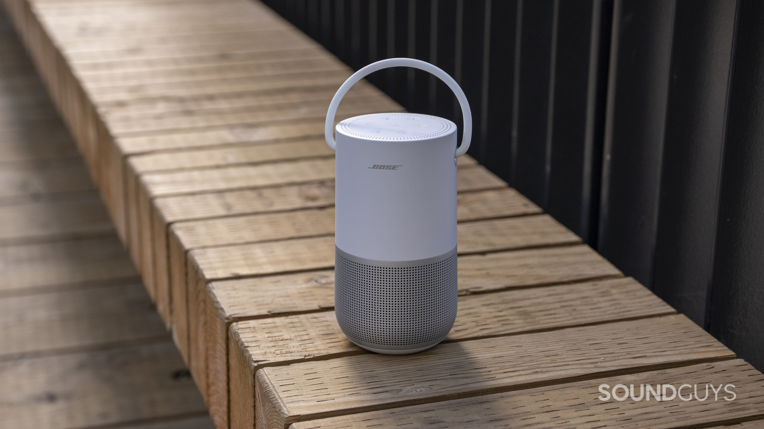A Bose Portable Smart Speaker sitting on a wooden bench outdoors.
