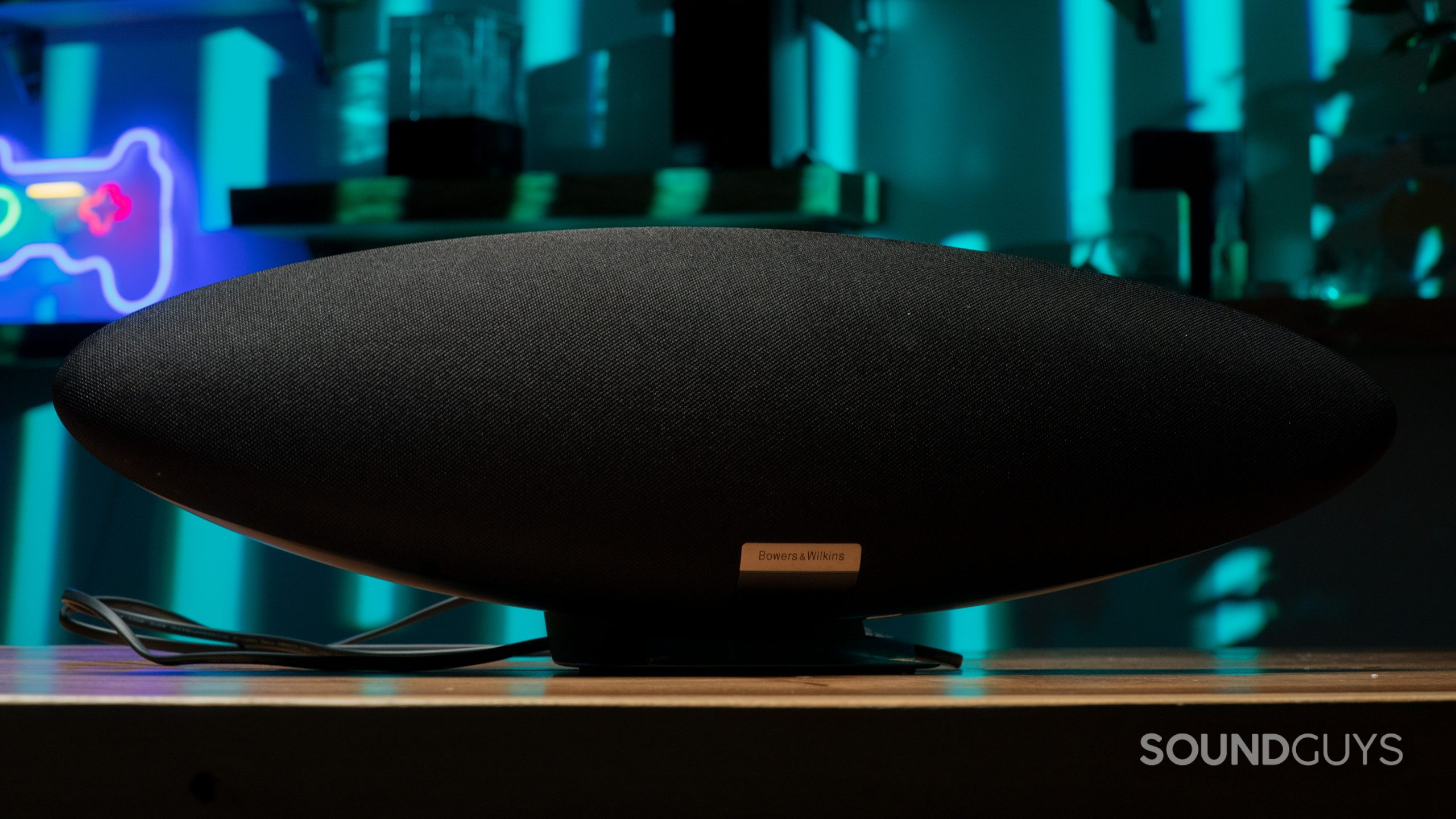 A black Bowers &amp; Wilkins Zeppelin shown resting on a table in front of an abstract background of light blue and black shapes.