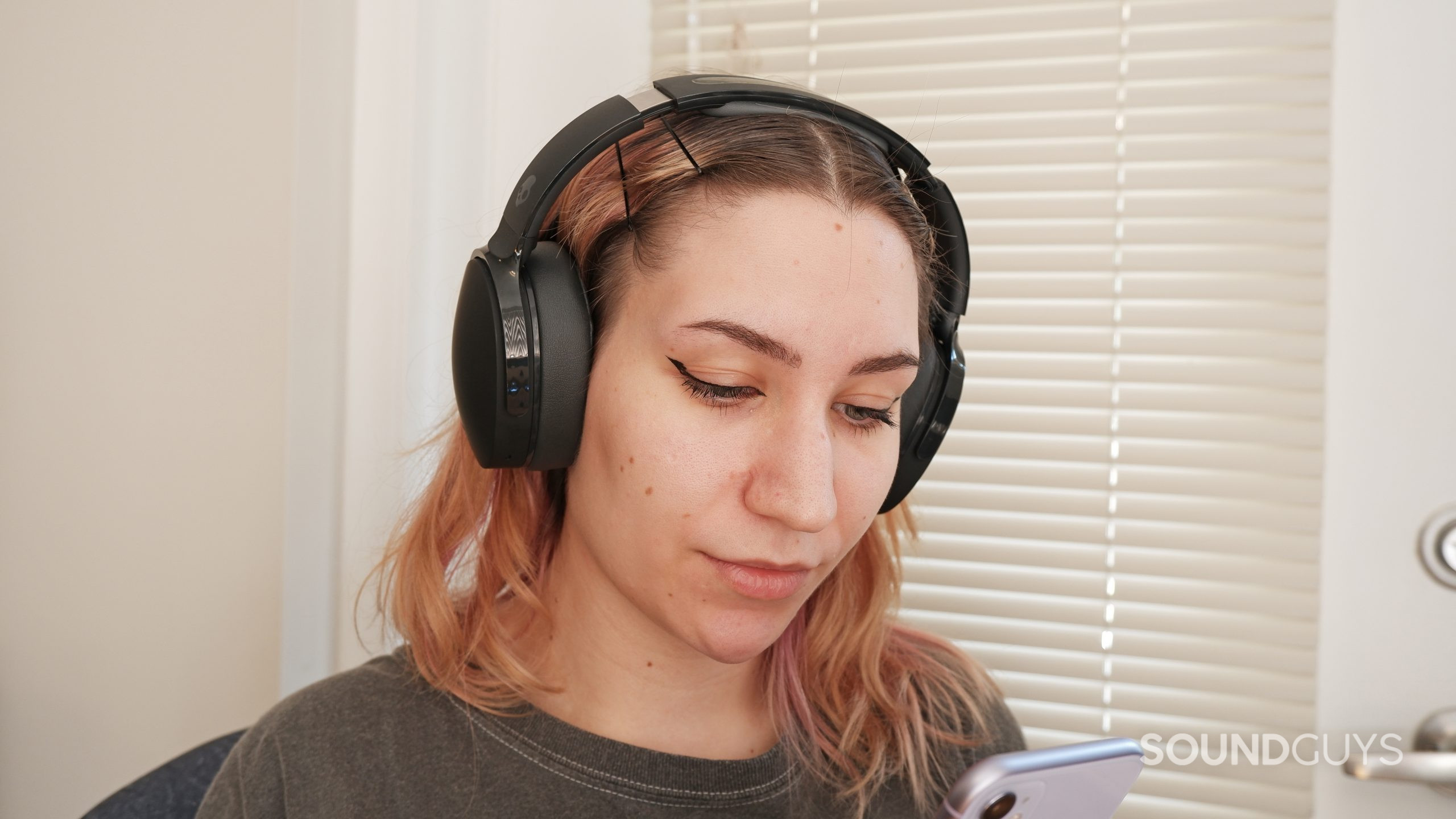 A woman wearing the Skullcandy Hesh ANC while looking down at her phone.