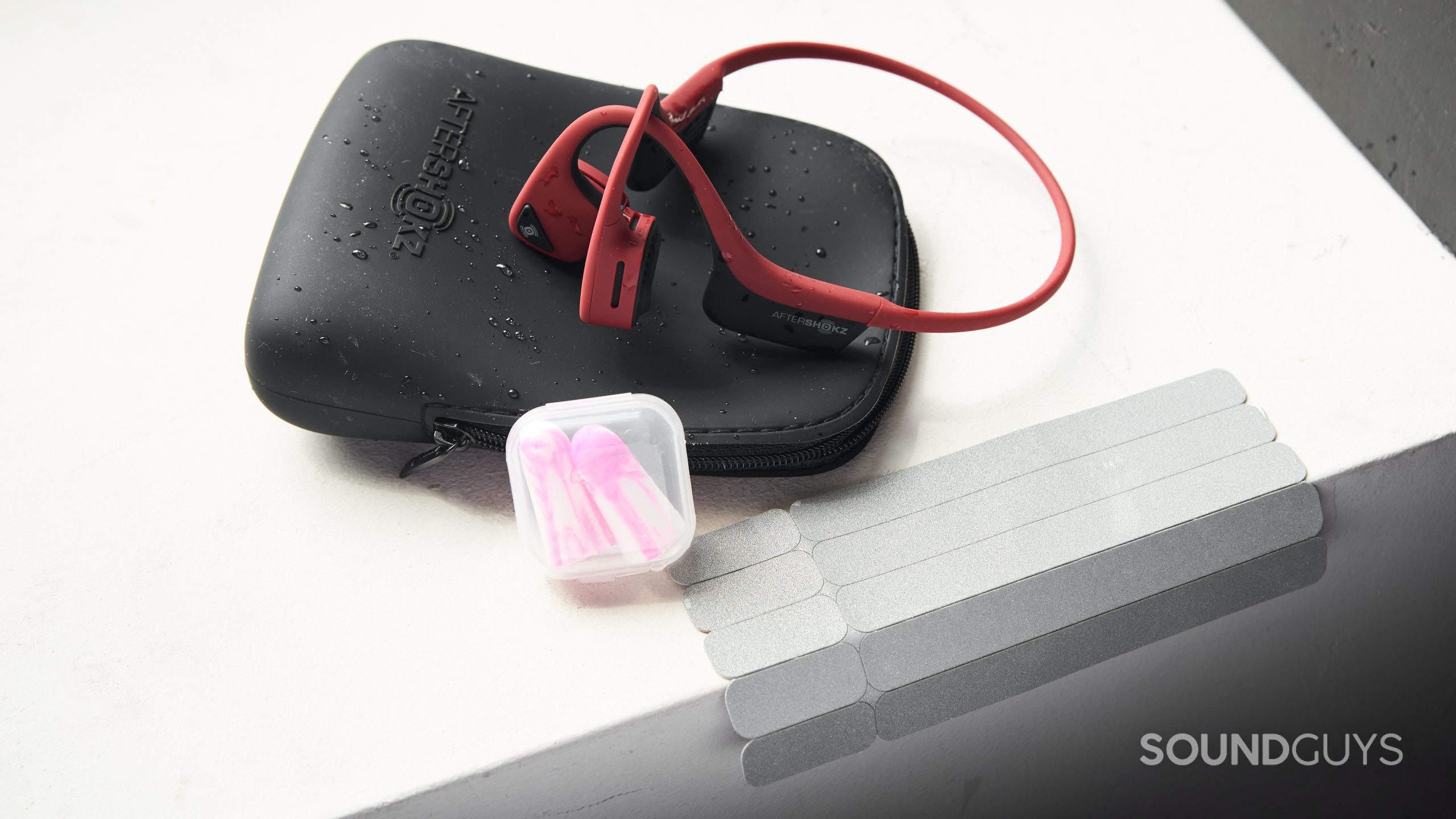 The AfterShokz Air bone conduction headphones, ear plugs, carrying case, and reflective stickers all next to each other.