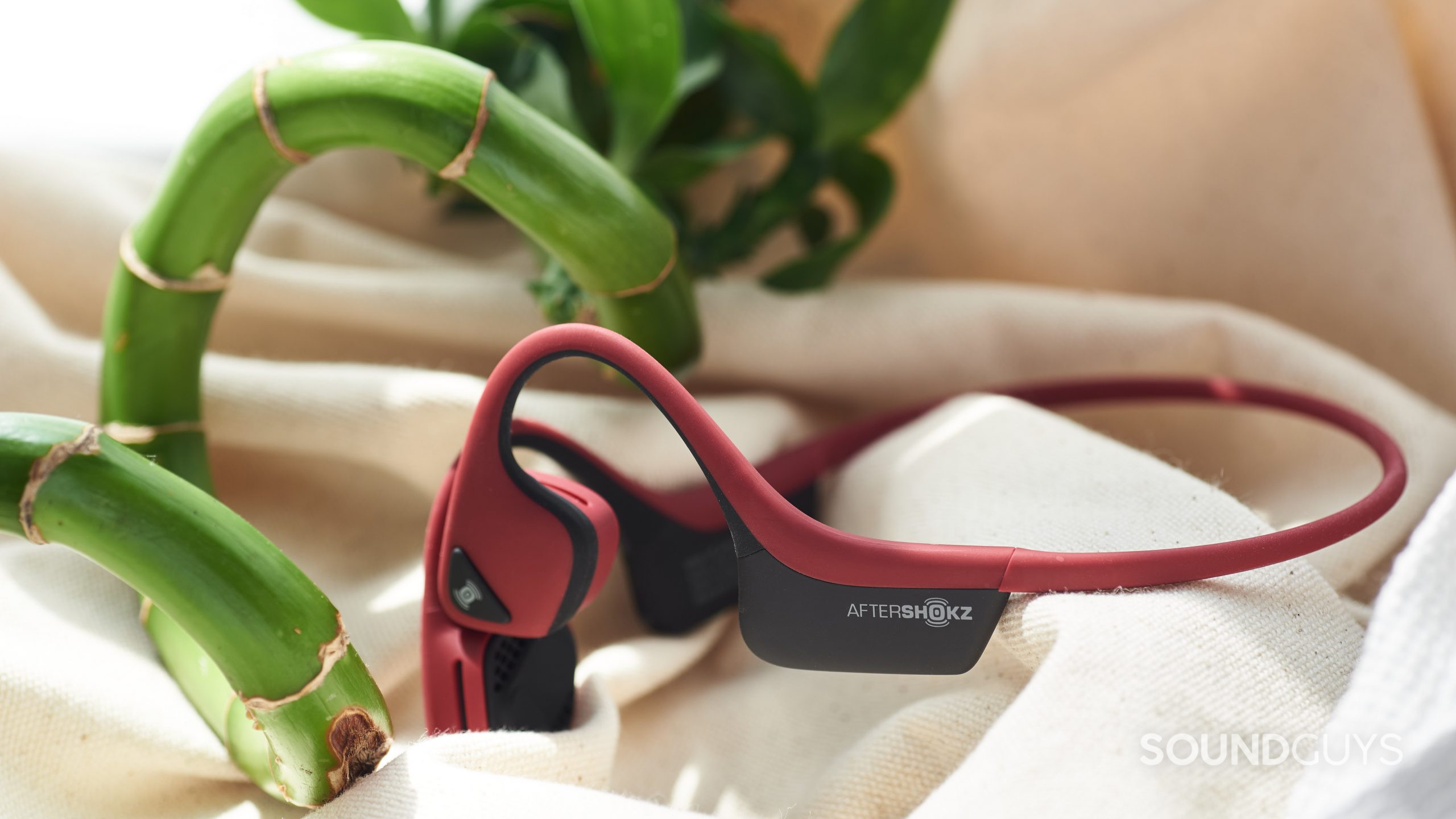 The AfterShokz Air bone conduction headphones lay on a cloth surface next to a bamboo stick.