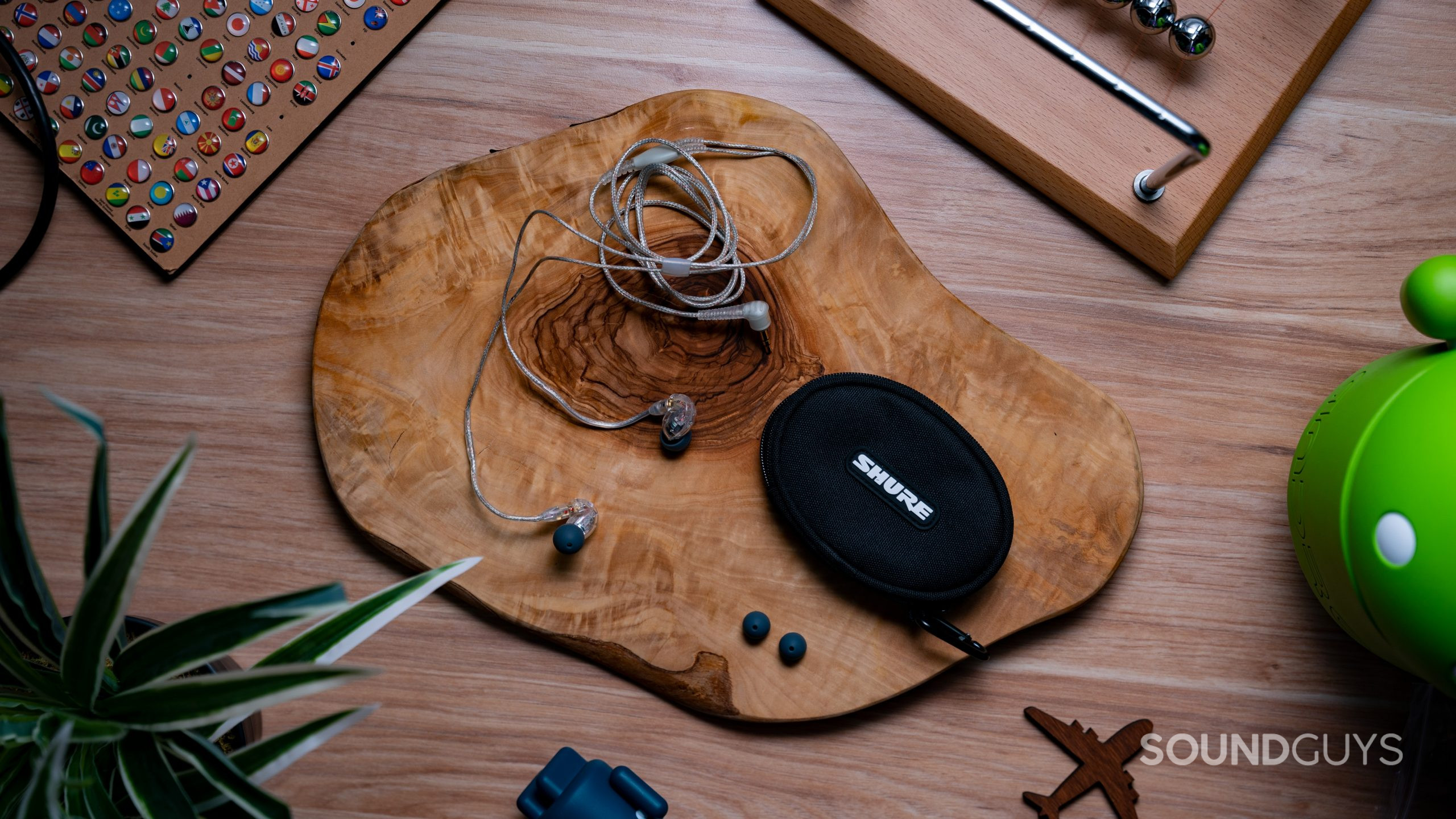 On a wood surface the Shure SE215 rests with its case, an extra set of ear tips.