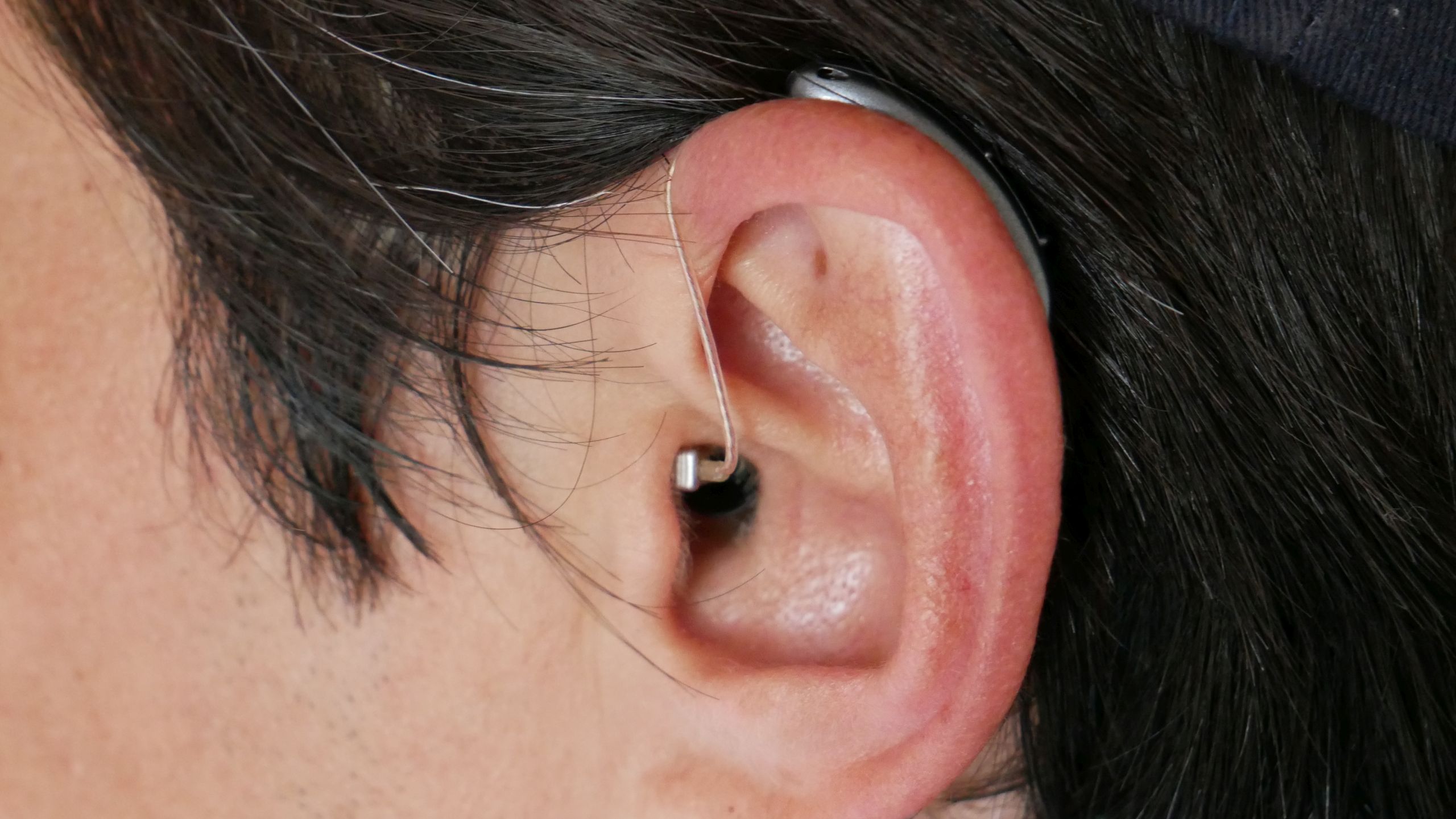 Side-view of a white man's left ear with the receiver of a with a Signia Pure Charge&amp;Go AX behind-the-ear hearing aid extending into the ear canal.