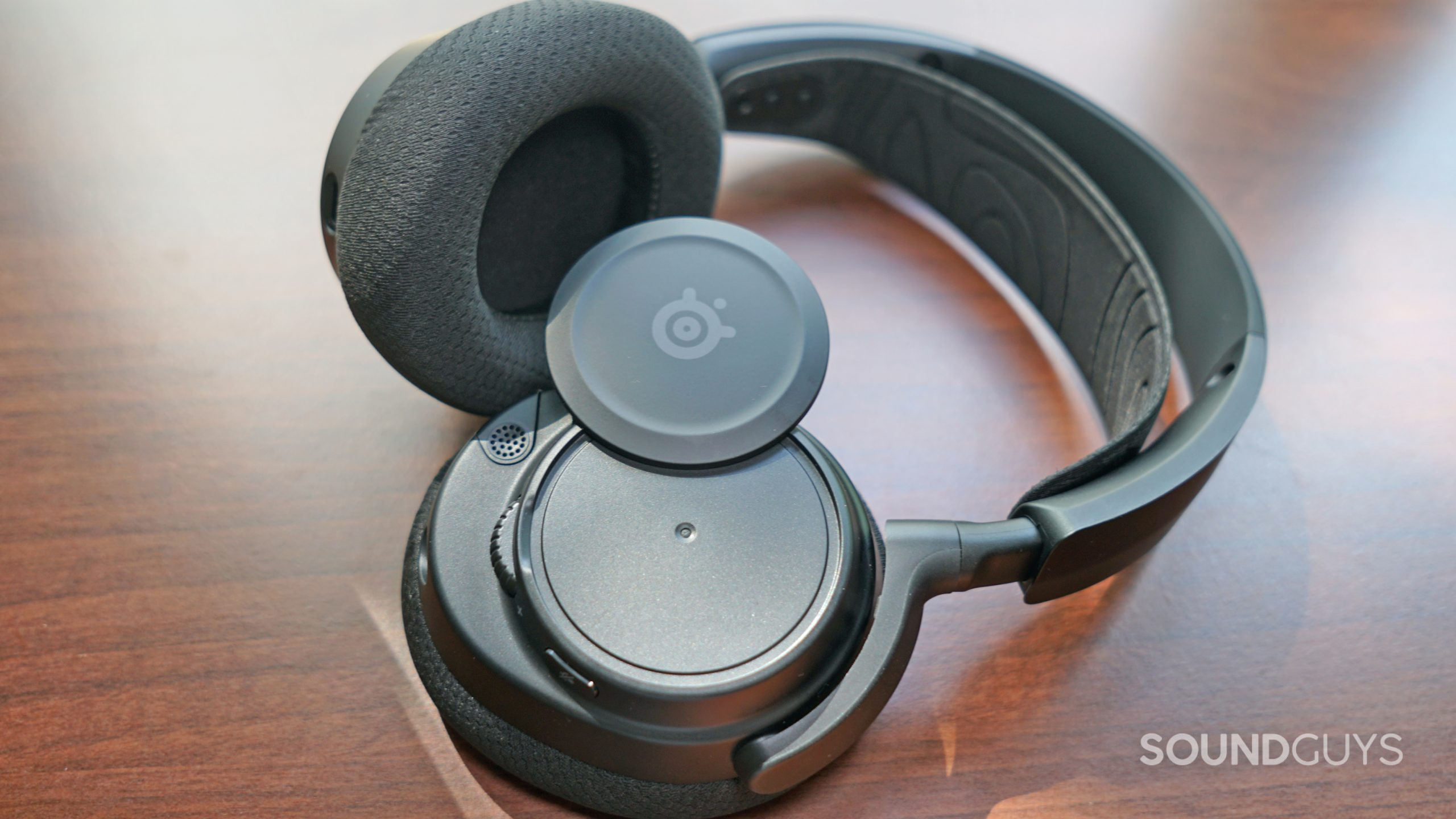 The SteelSeries Arctis Nova 7 lays on its side, with its side plates partially off.