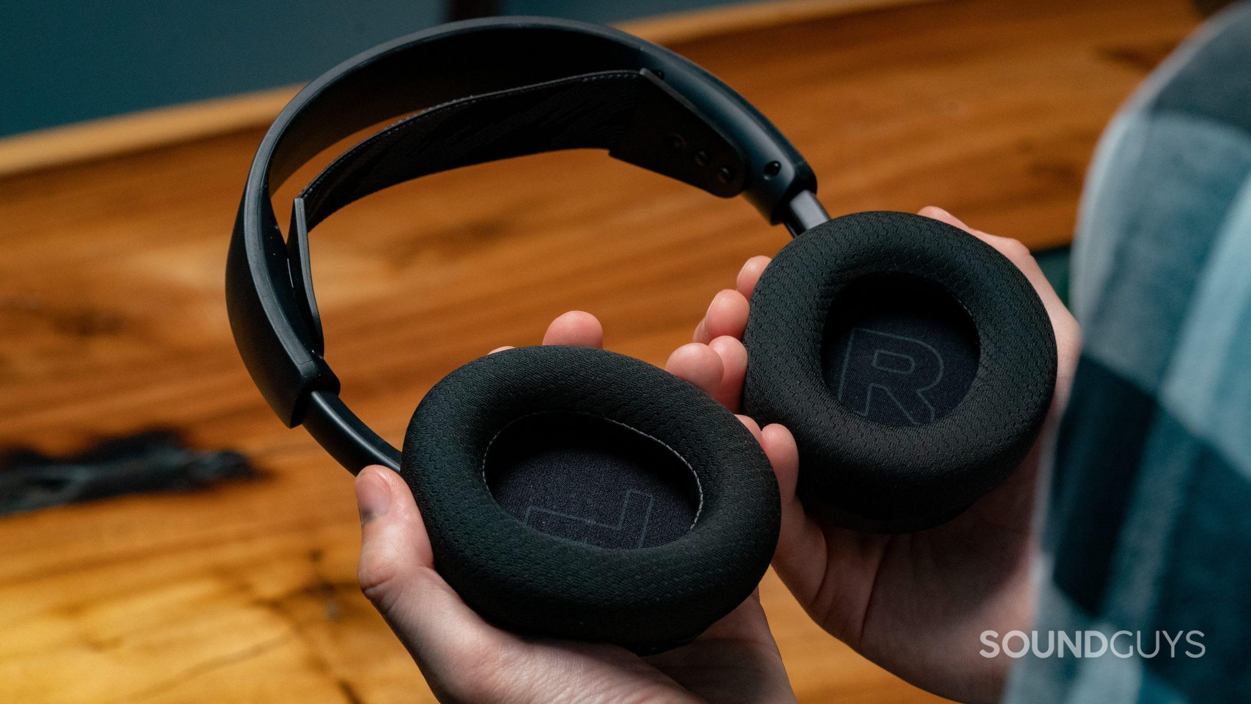 The SteelSeries Arctis Nova 1 being held in a user's hands with a wooden table as a backdrop.