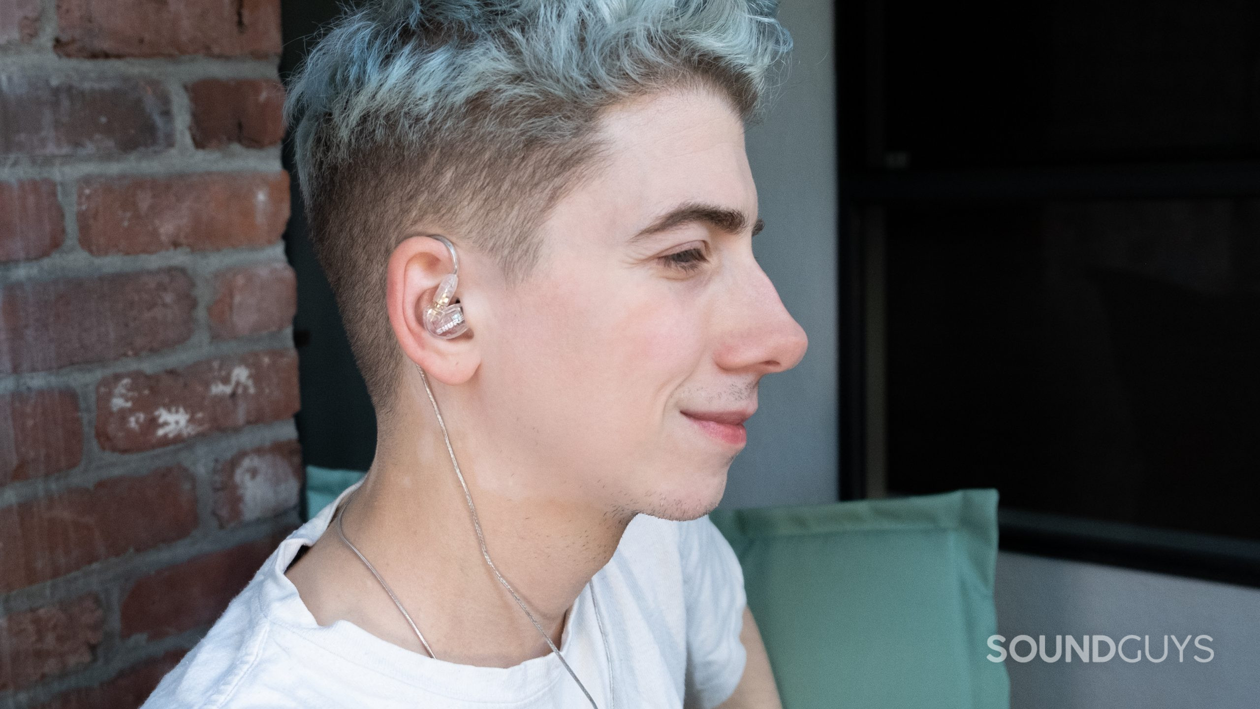 A man faces right wearing the Shure SE215 cabled around the top of the ear with the cable running down behind the back of his ear.