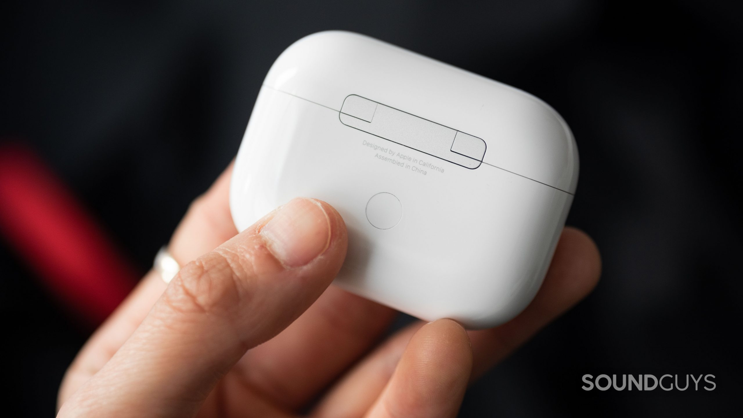 A hand holds the Apple AirPods Pro (2nd generation) case with the pairing button in full view.