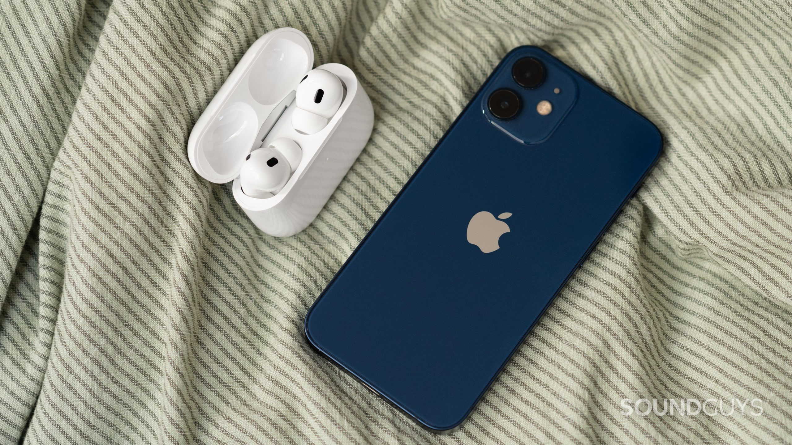 Apple AirPods Pro (2nd generation) true wireless earbuds open case iphone 12 mini The Apple AirPods Pro (2nd generation) case open with the earbuds next to an iPhone 12 mini.