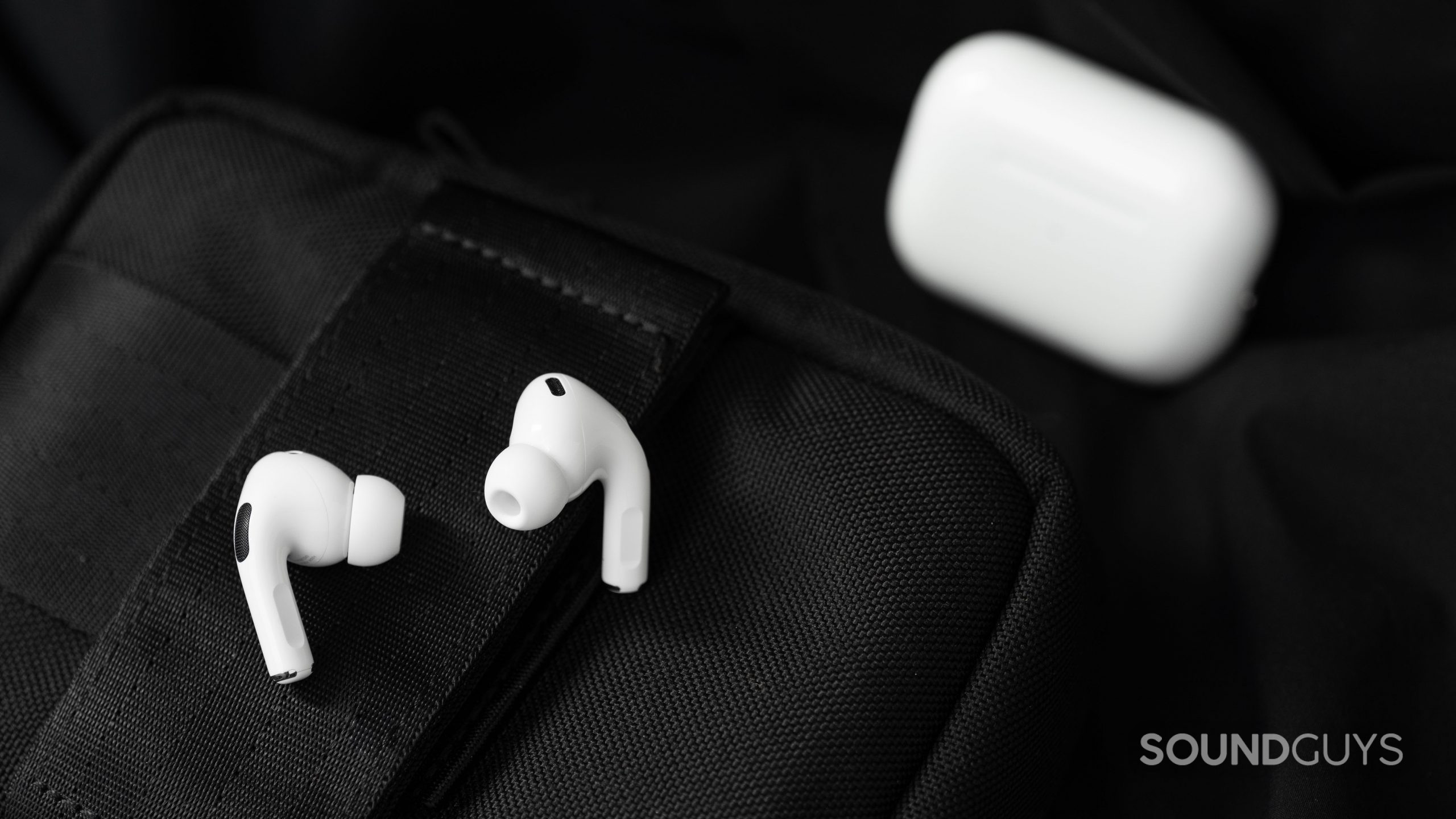 The Apple AirPods Pro (2nd generation) earbuds rest on a black surface with the case in the background.