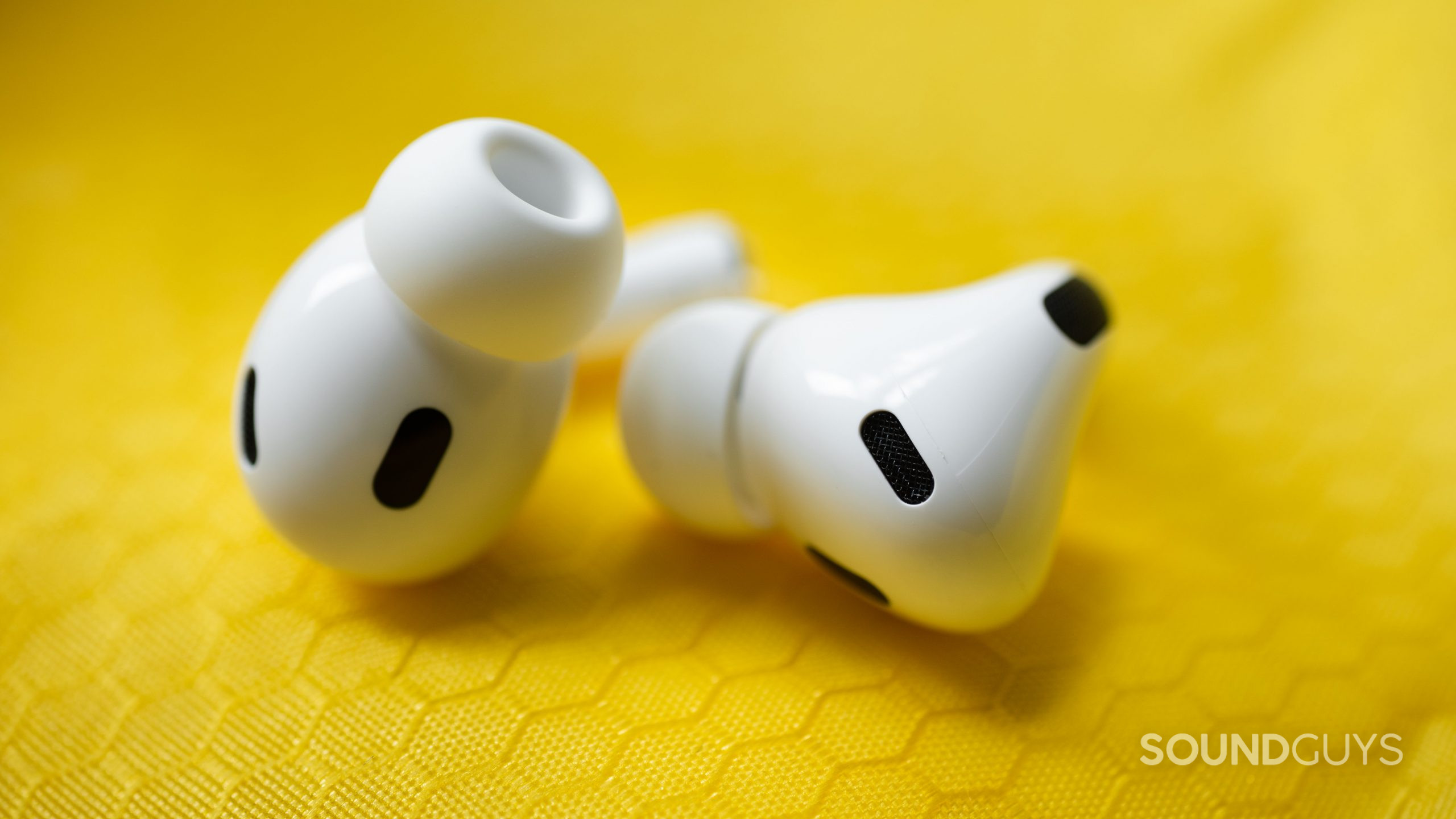 The Apple AirPods Pro (2nd generation) sensors decorate the earbuds which lay on a yellow, textured surface.