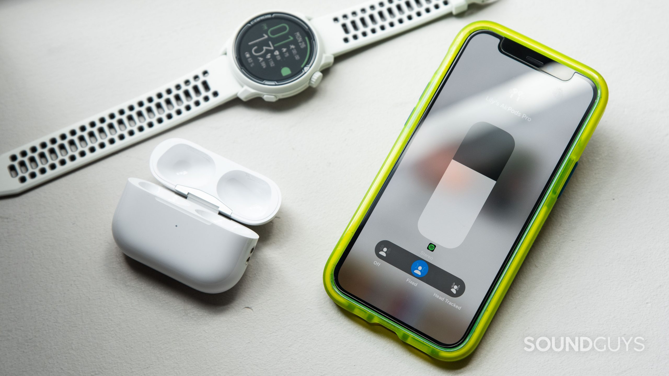 An iPhone 12 mini displays the AirPods Pro (2nd generation) spatial audio modes with the case and a smart watch next to it.