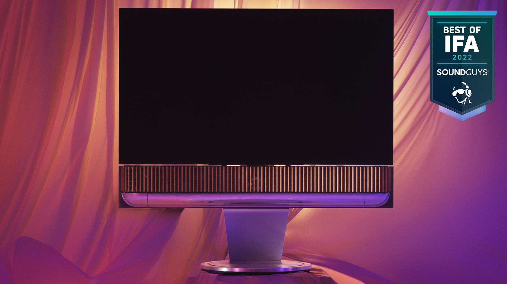 Bang & Olufsen Beosound Theatre soundbar TV stand IFA The Bang & Olufsen soundbar/TV stand connected to a TV against a magenta fabric background.