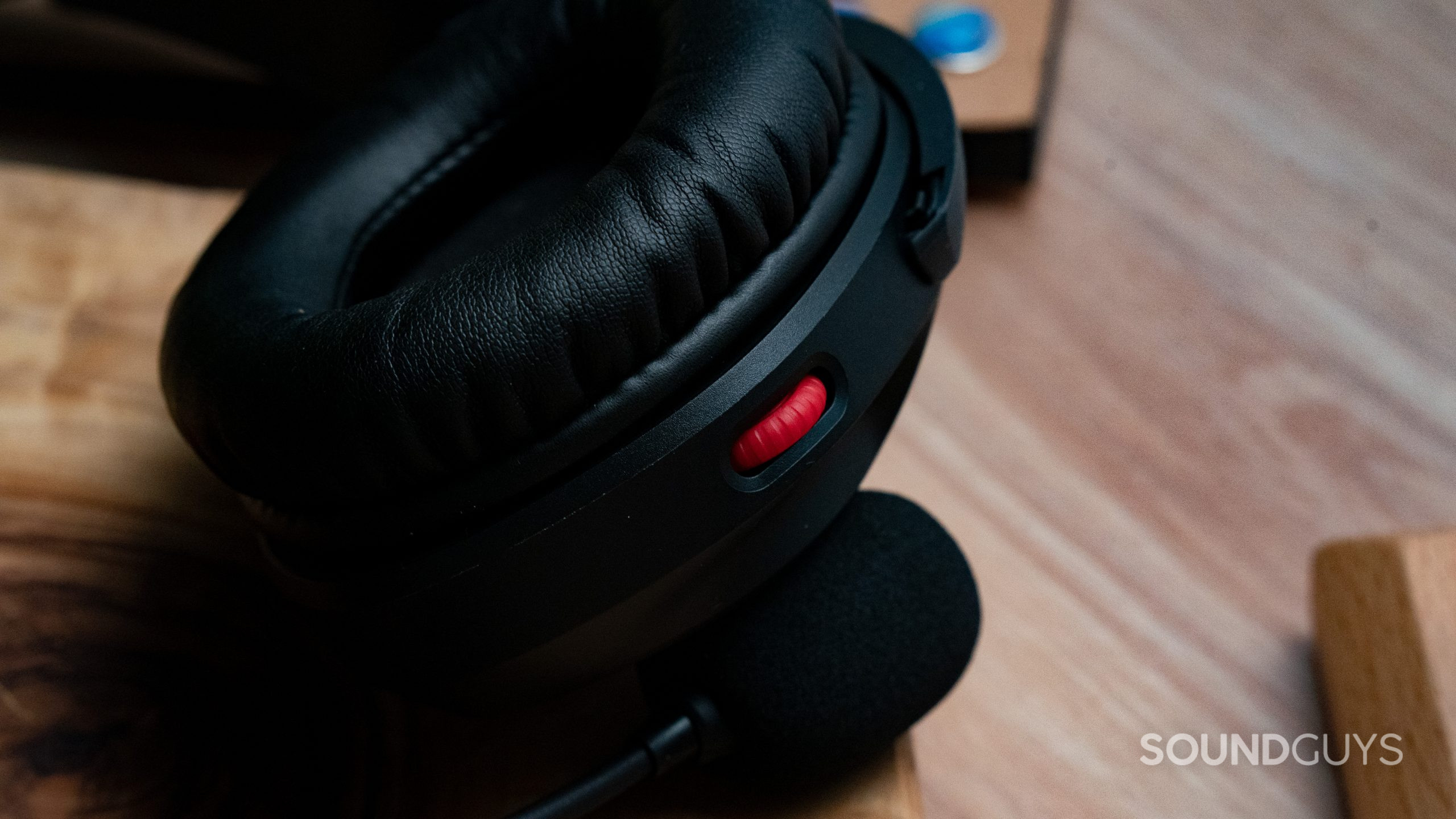 The HyperX Cloud Stinger 2's red volume knob in closeup with a wooden table in the background.