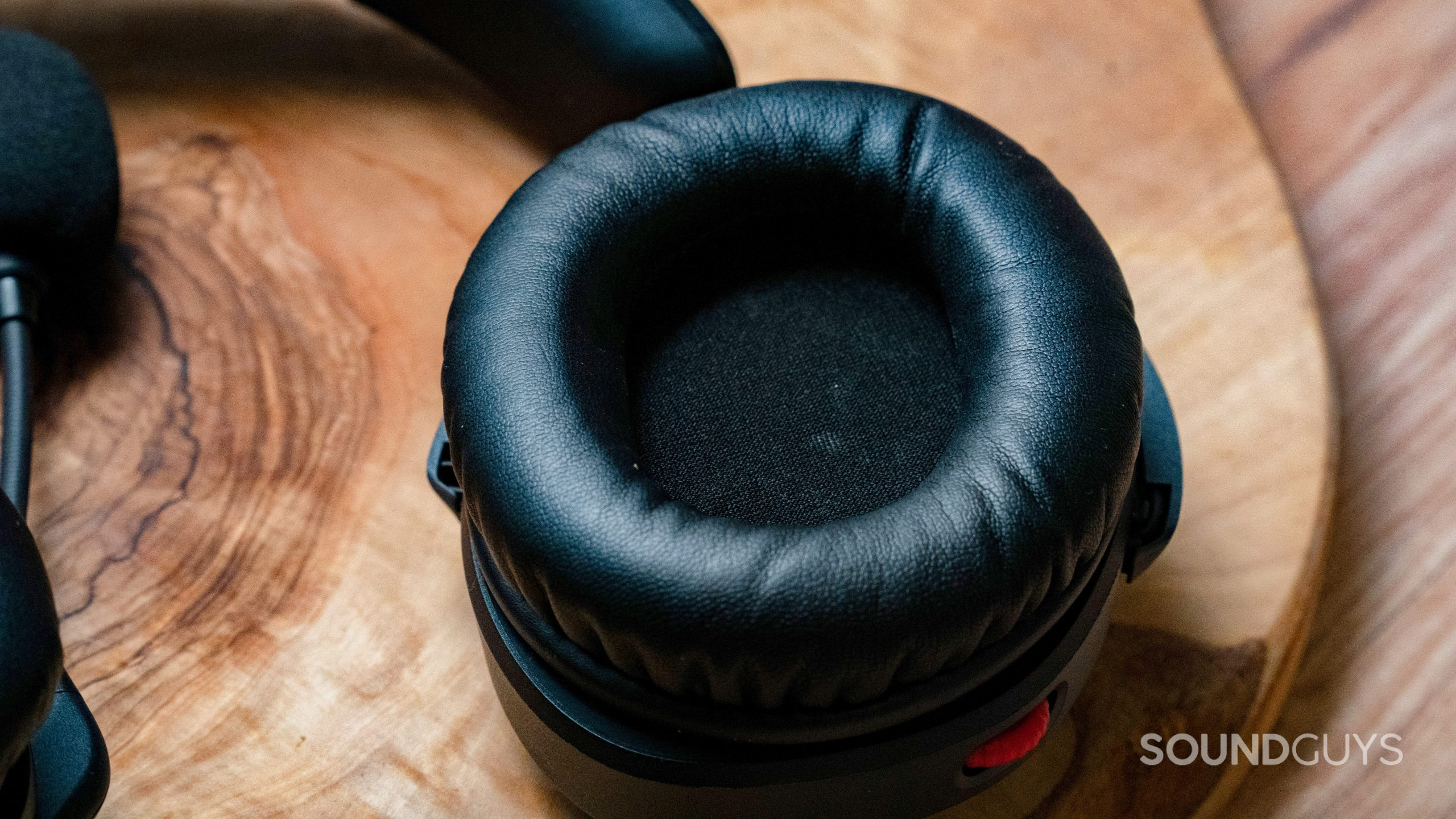 The HyperX Cloud Stinger 2's ear cup with black pleather material on top of a wooden tabletop.