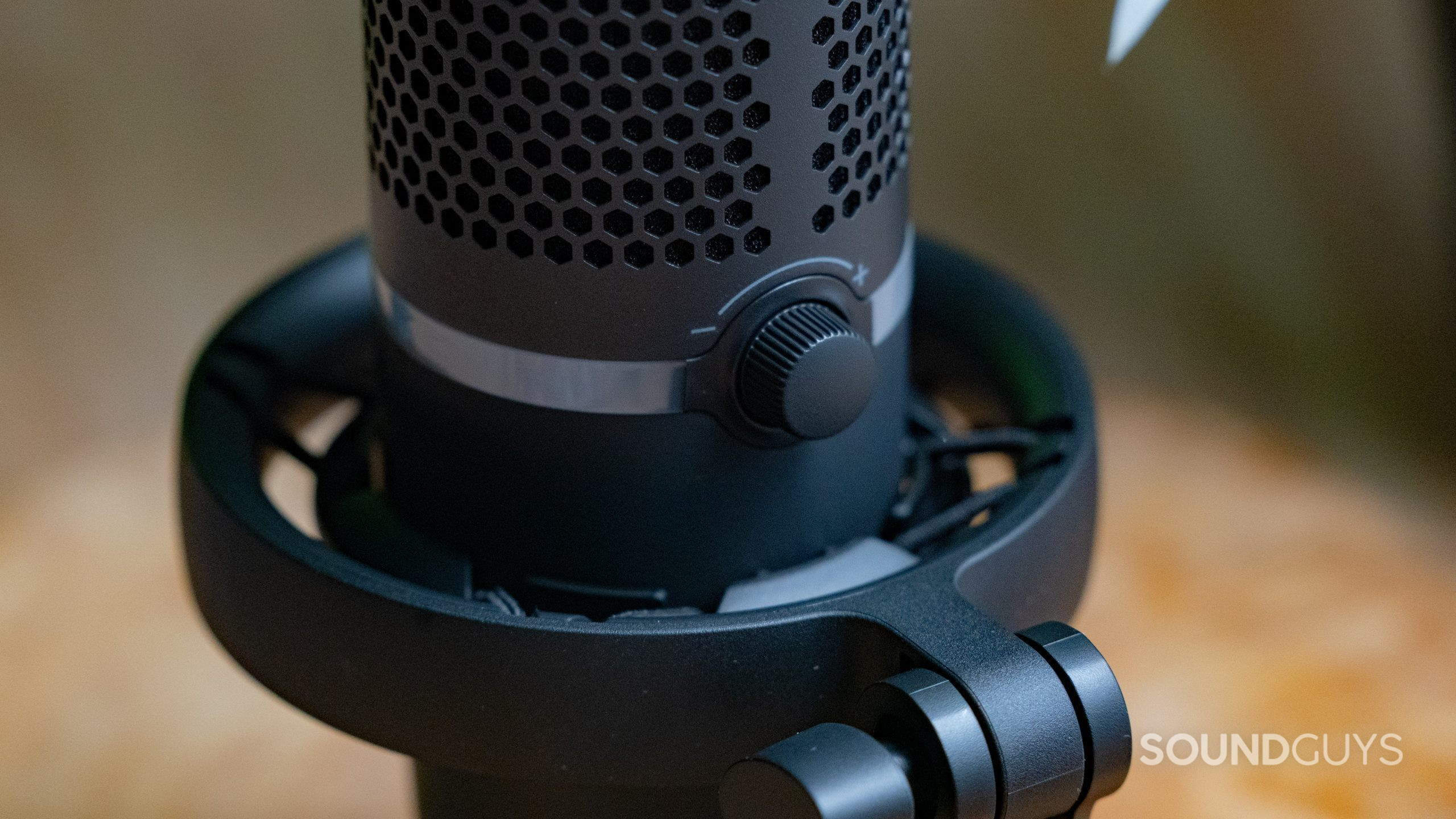 A close up of the HyperX DuoCast's volume knob and mounting system with a wooden table in the background.