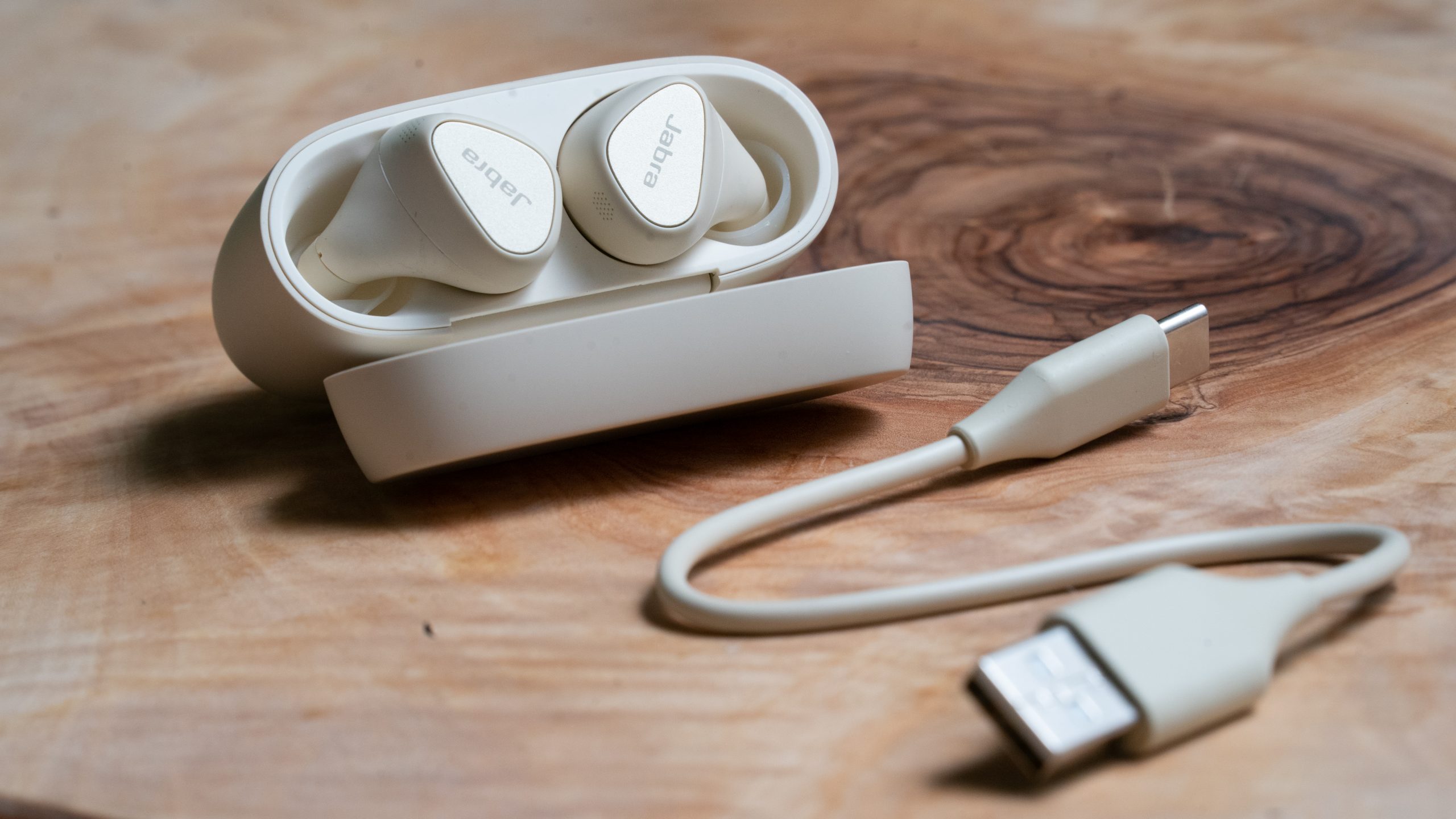 The Jabra Elite 5 true wireless earbuds in white on a wooden surface with the case open.