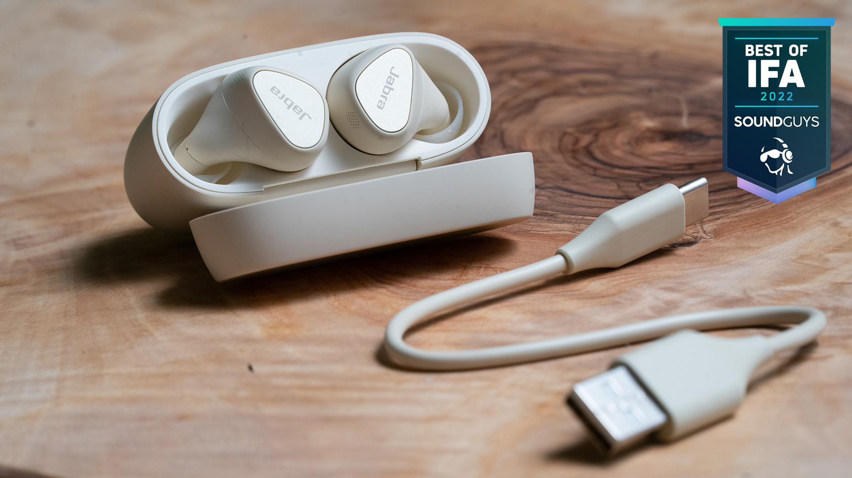 The Jabra Elite 5 true wireless earbuds in white on a wooden surface with the case open.The Jabra Elite 5 true wireless earbuds in white on a wooden surface with the case open.