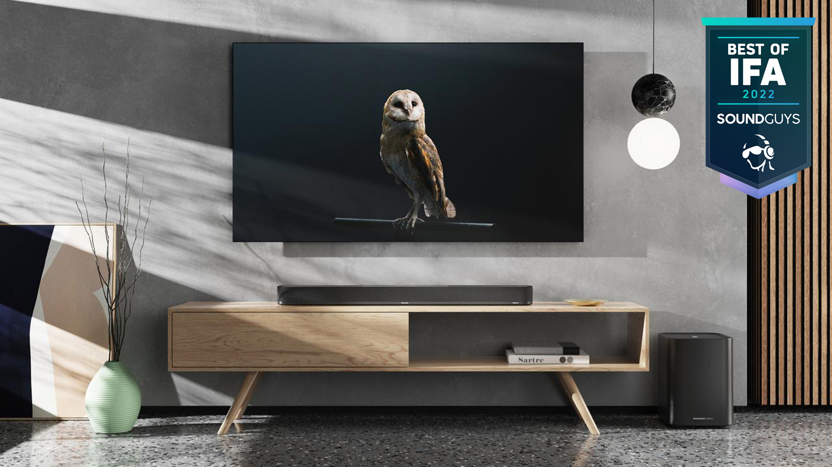 Sennheiser Ambeo Plus soundbar living room IFA badge The Sennheiser AMBEO Plus soundbar in a living room setting with the separate sub-woofer on the floor.