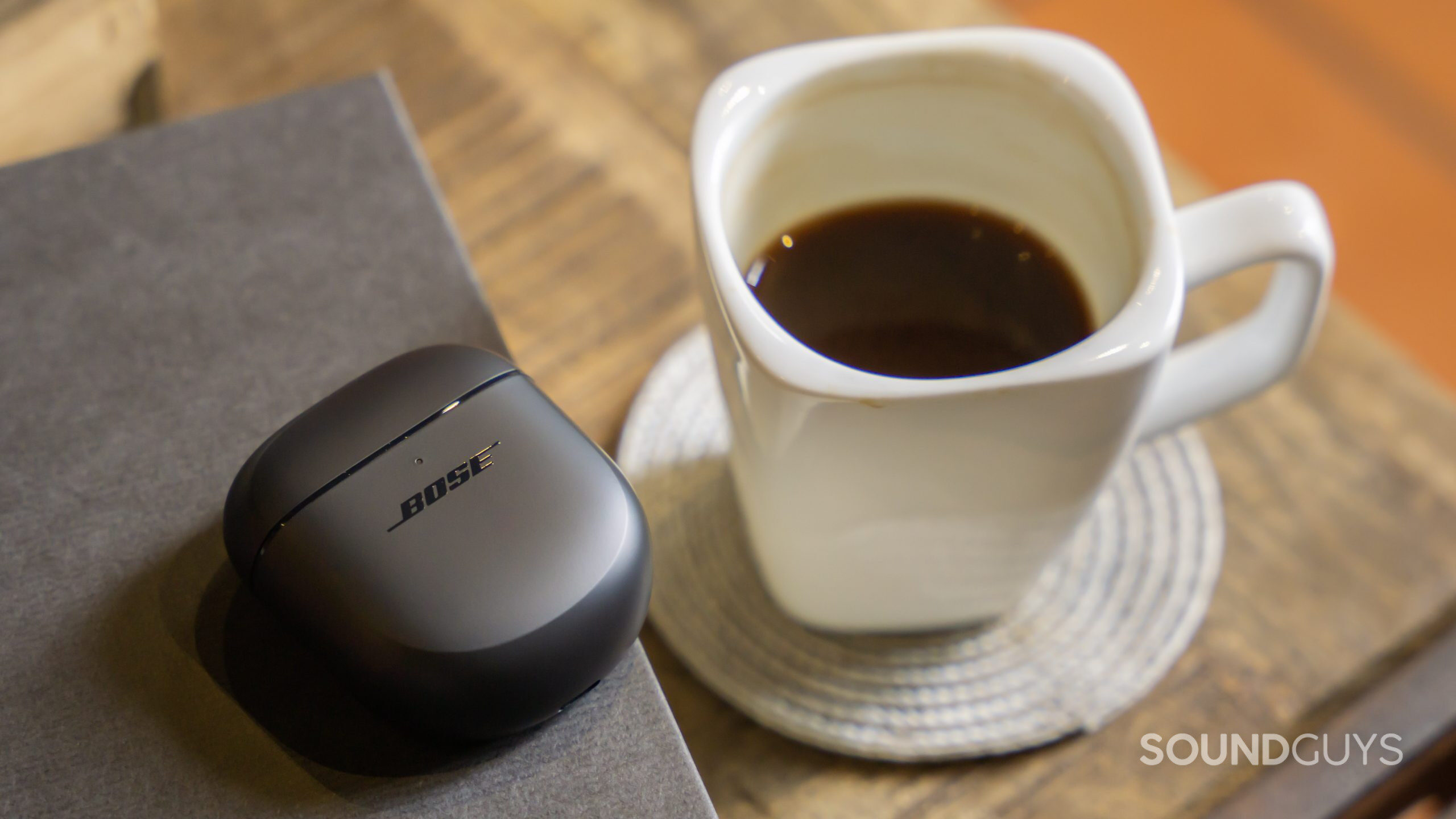 The Bose QuietComfort Earbuds II case rests next to a table and coffee mug.