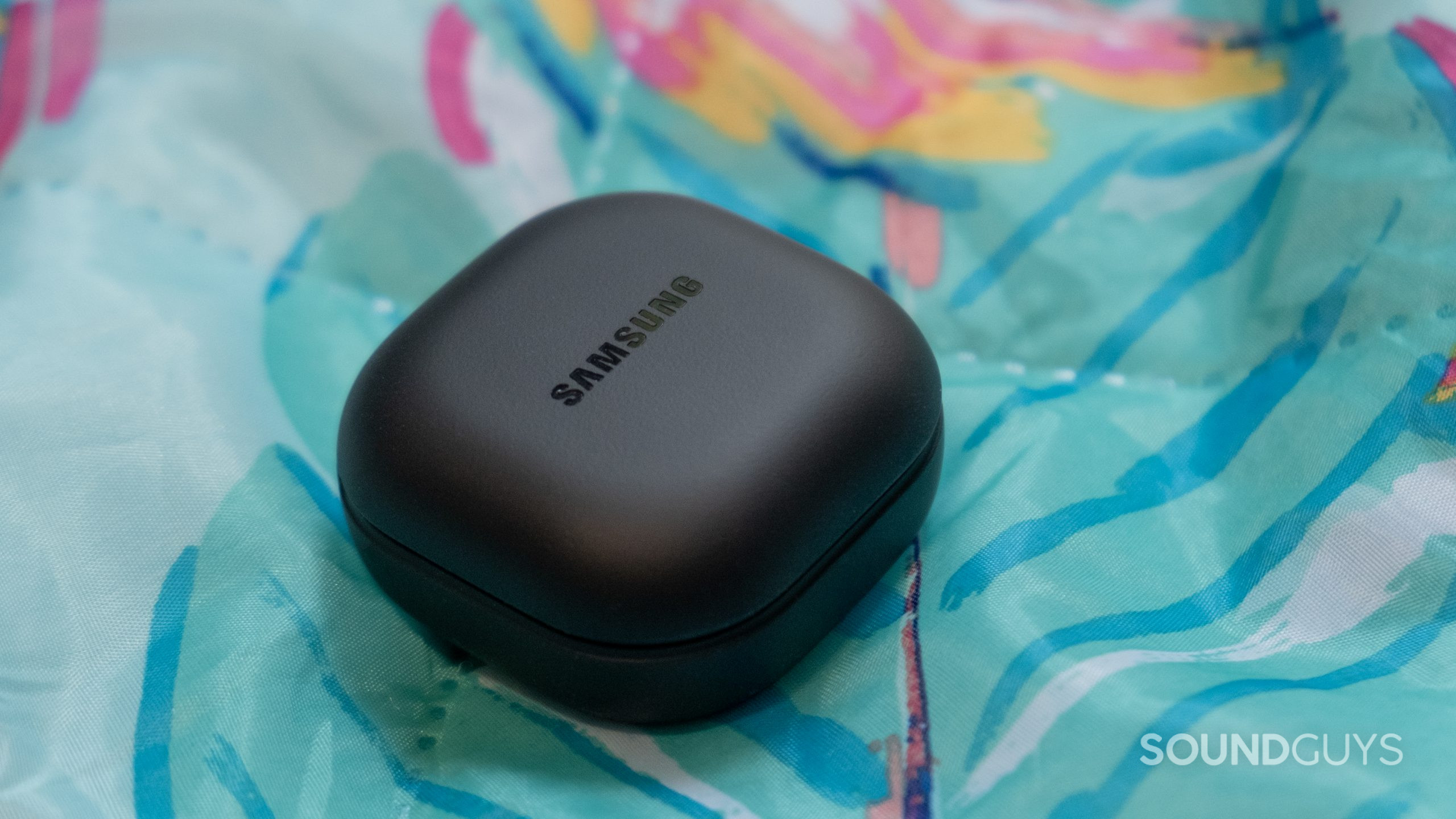 The closed back case of the Samsung Galaxy Buds 2 Pro rests on a colorful tropical themed blanket.
