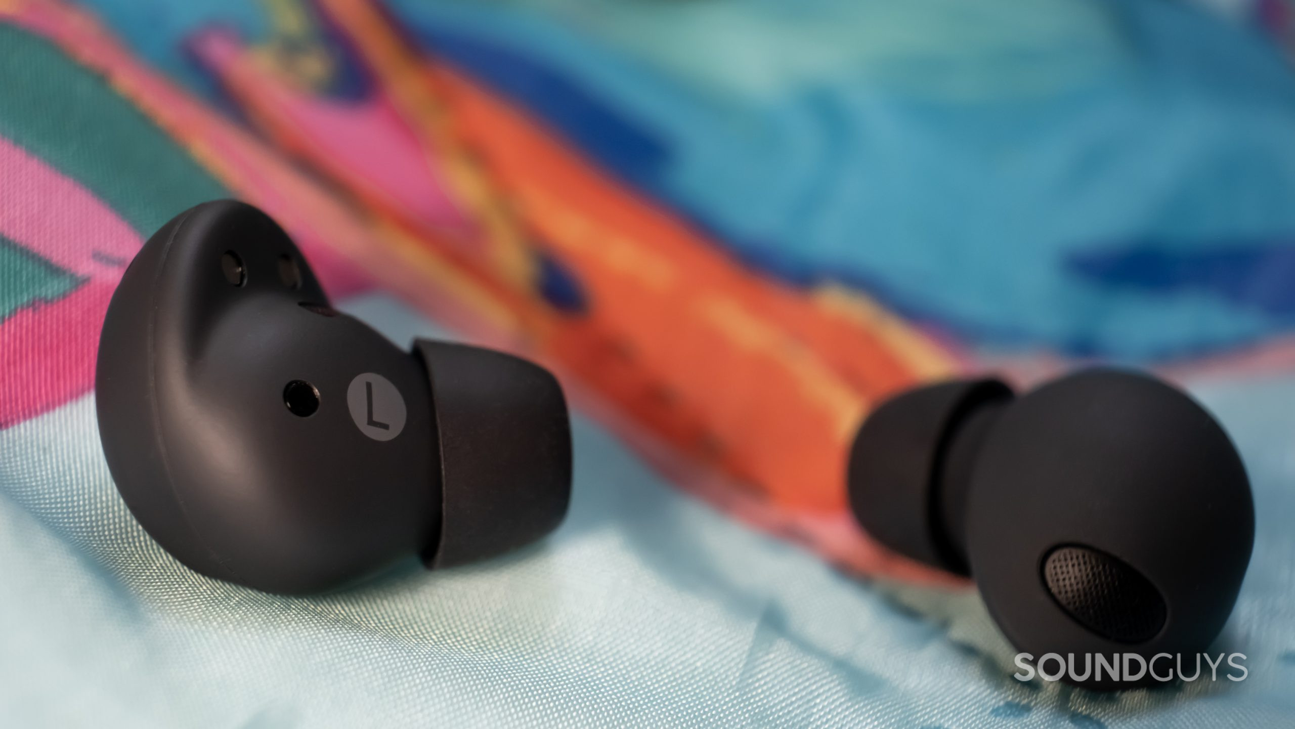 A macro close up of the Samsung Galaxy Buds 2 Pro shows the inner and outer housing, including the ear tips and vent, while resting on a colorful blanket.