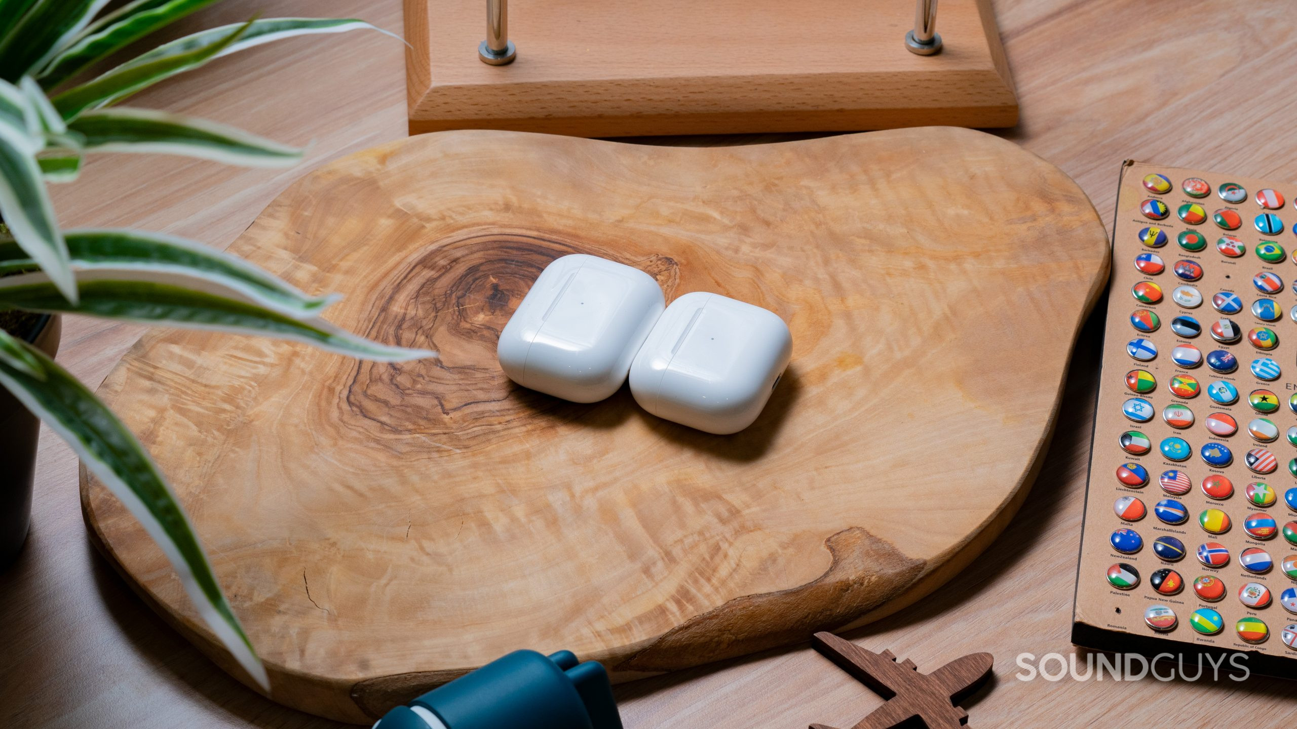 The cases of the Apple AirPods Pro Gen 2 and the Apple AirPods Gen 3 sitting side by side on a wooden table.