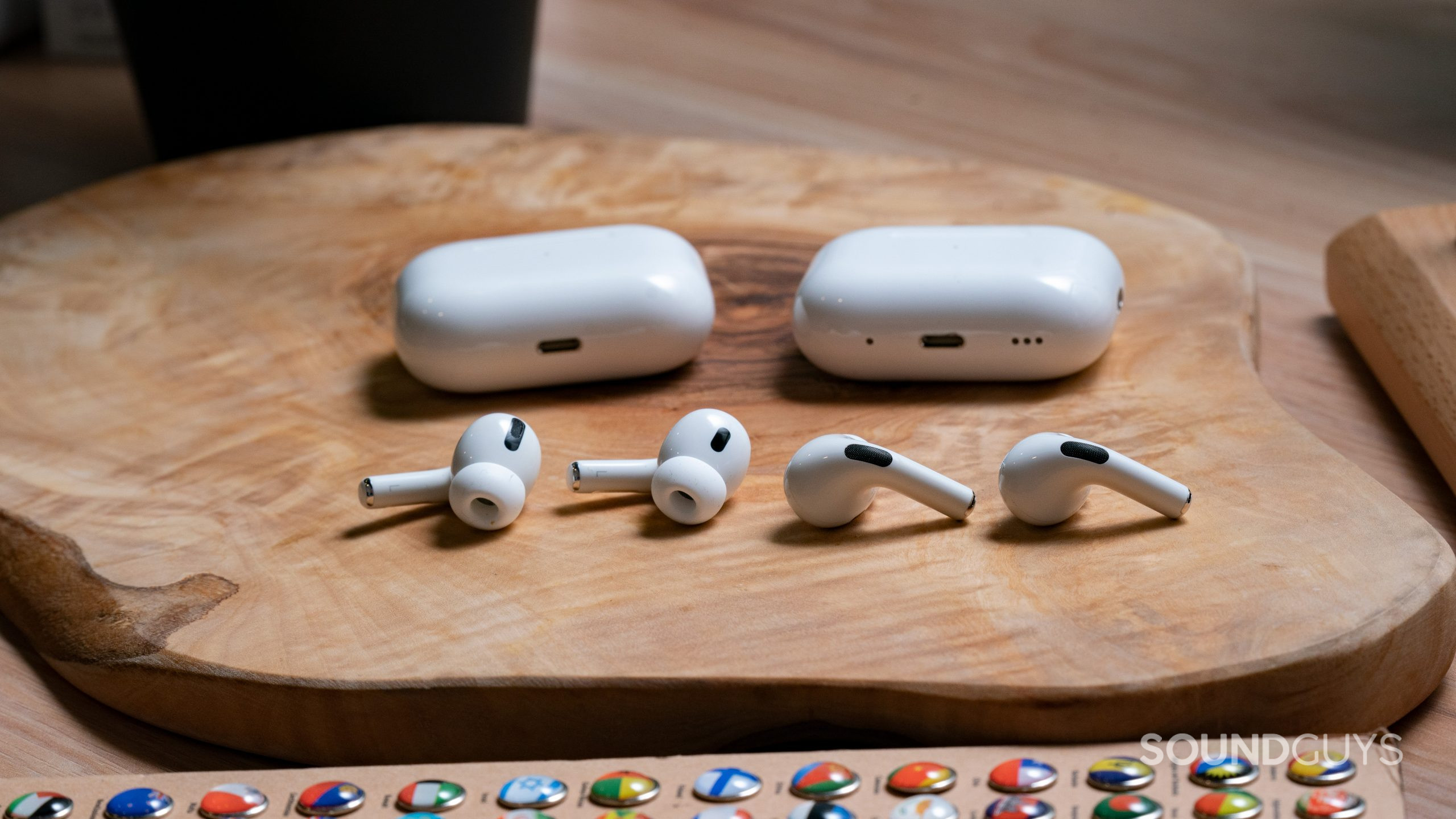 The Apple AirPods Pro (2nd generation) lays on a wooden surface next to the Apple AirPods Pro (1st generation), earbuds out of case.