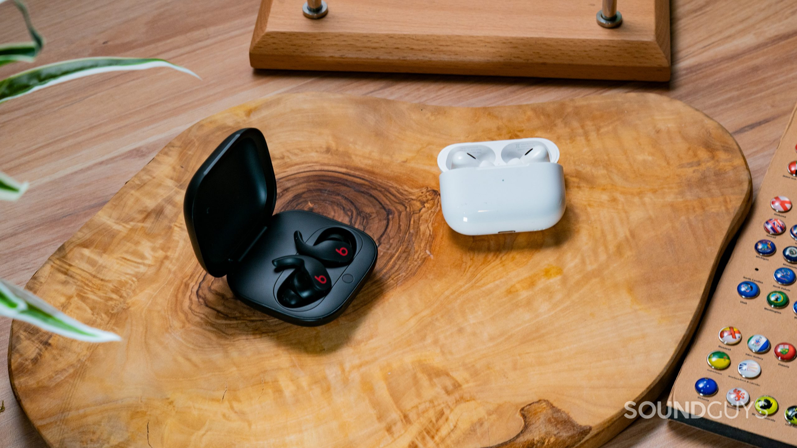 Apple Airpods Pro Gen 2 vs. Beats Fit Pro Hero Image The Beats Fit Pro and Apple AirPods Pro (2nd generation) next to each other in open cases on a wooden surface.