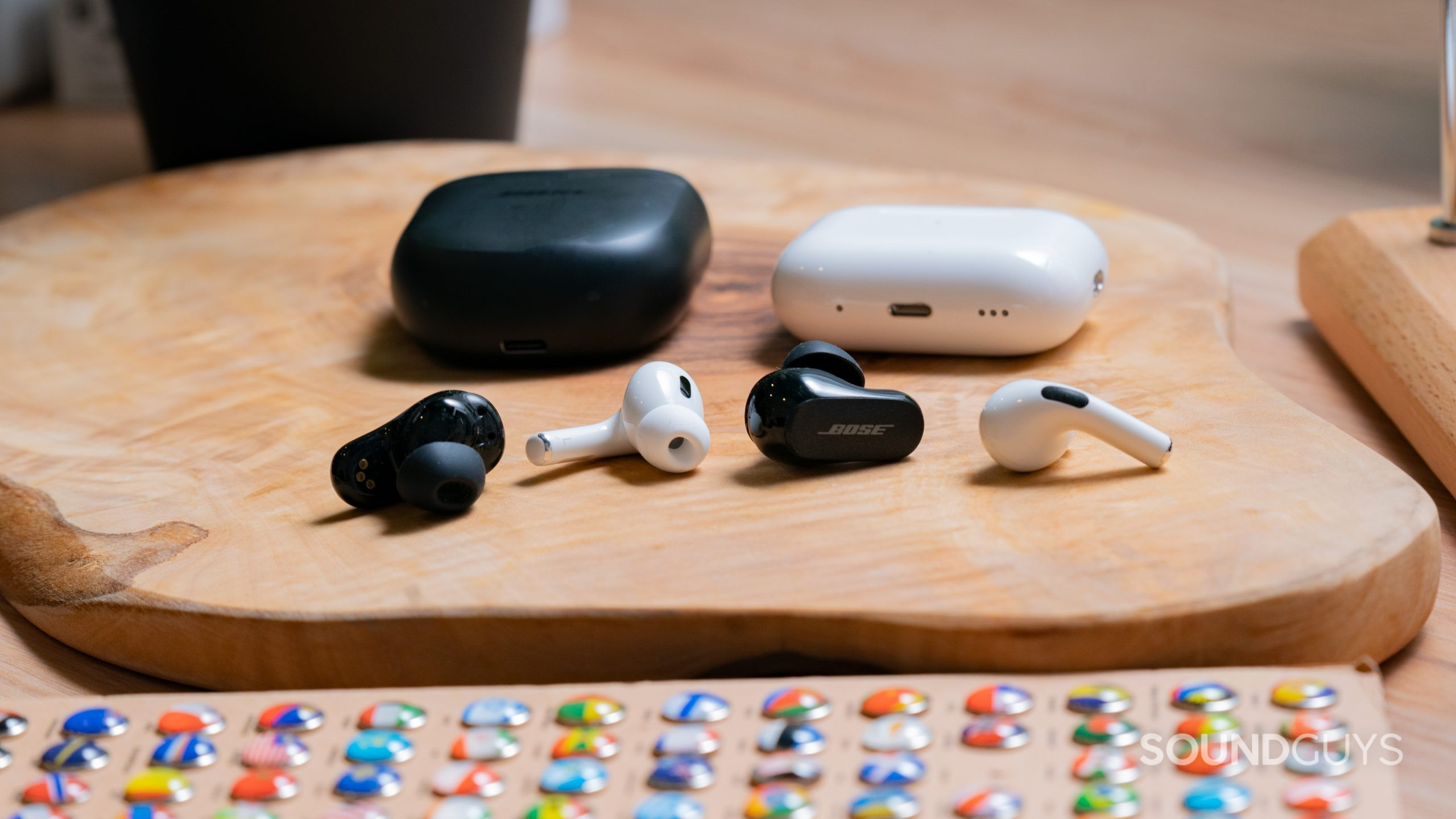 The earbuds and cases for the AirPods Pro (2nd generation) and the Bose QuietComfort Earbuds II beside each other on a wooden slab.