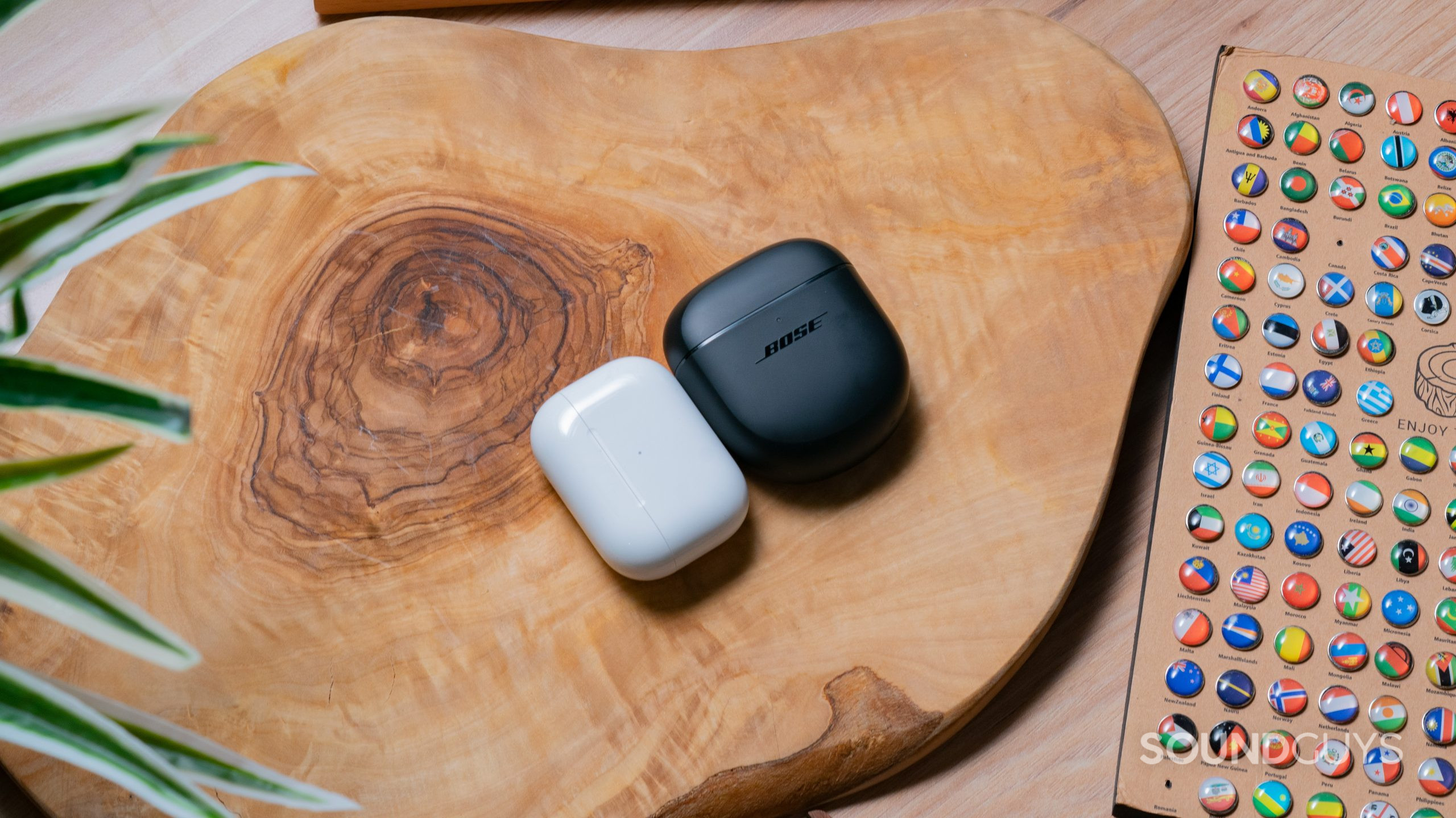 The AirPods Pro (2nd generation) and Bose QuietComfort Earbuds II cases beside each other on a wooden slab.