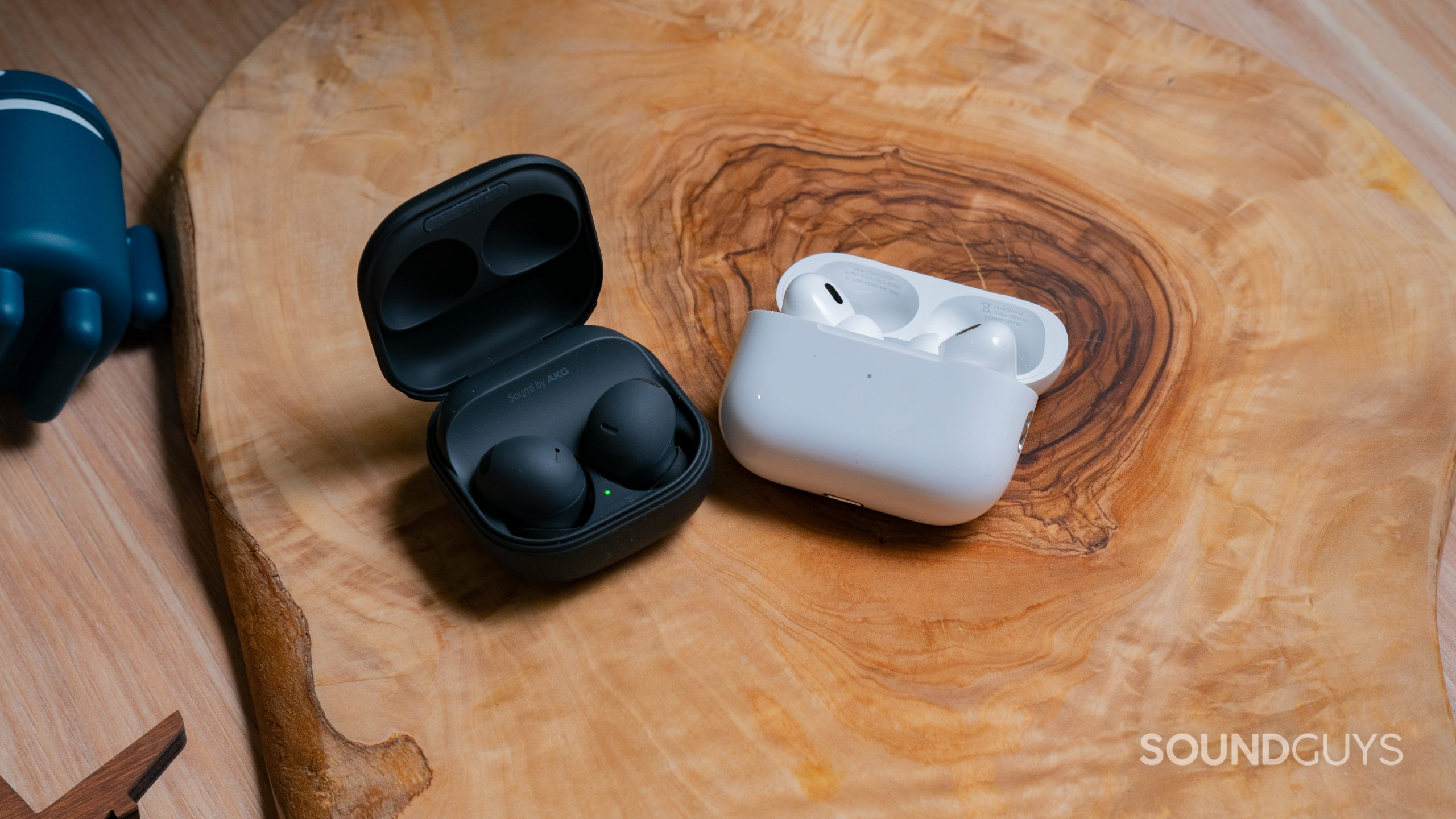 The open cases of the Samsung Galaxy Buds 2 Pro sit next to the Apple AirPods Pro (2nd generation) on a wood surface.