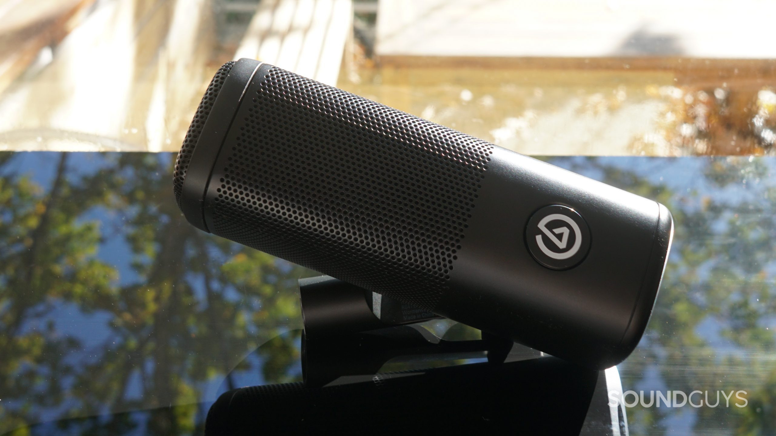 The Elgato Wave Dx mic lays on a black reflective surface next to a window