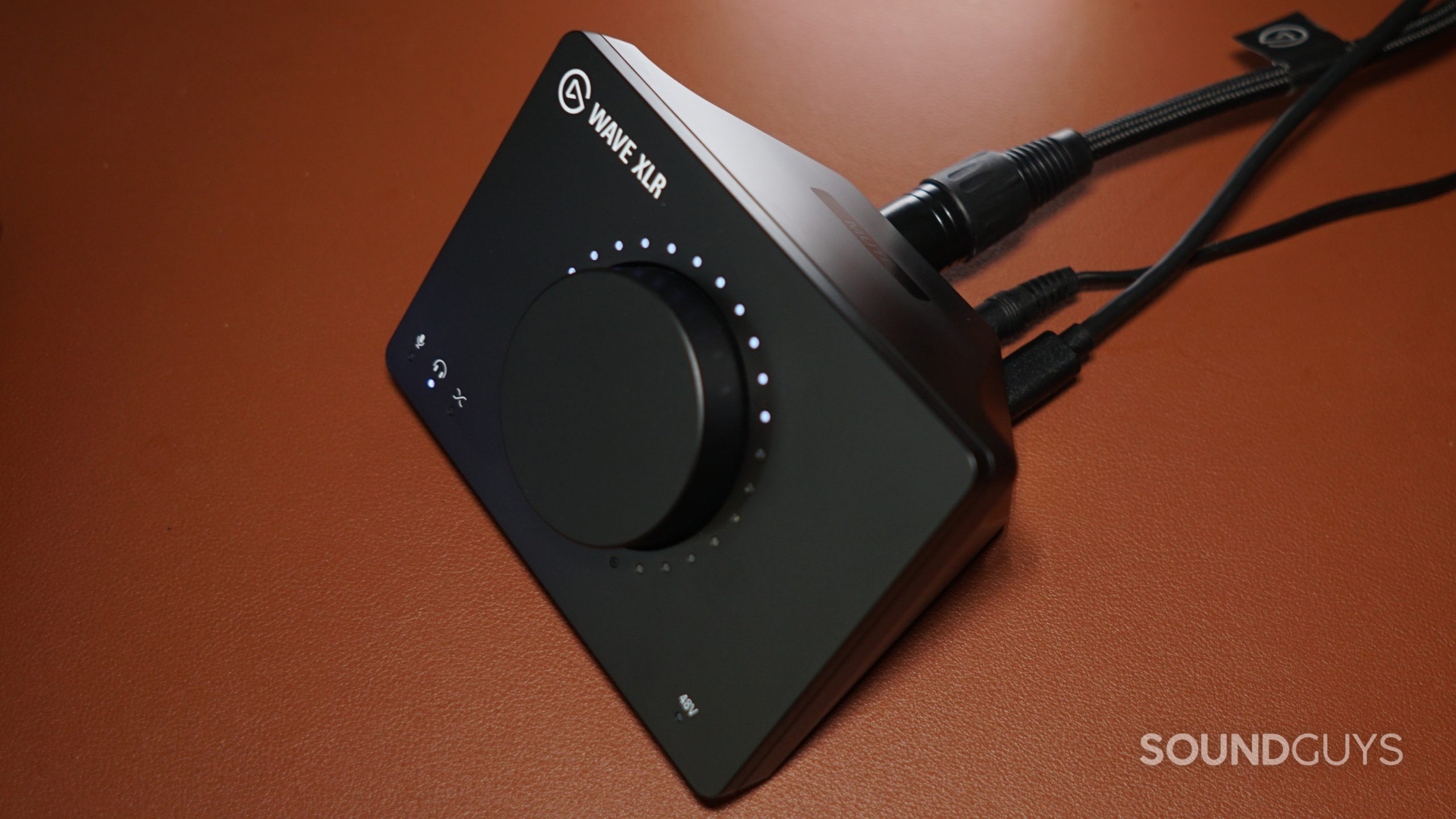 The Elgato Wave XLR unit sits on a leather surface, with cords plugged into its USB-C, XLR, and 3.5mm ports