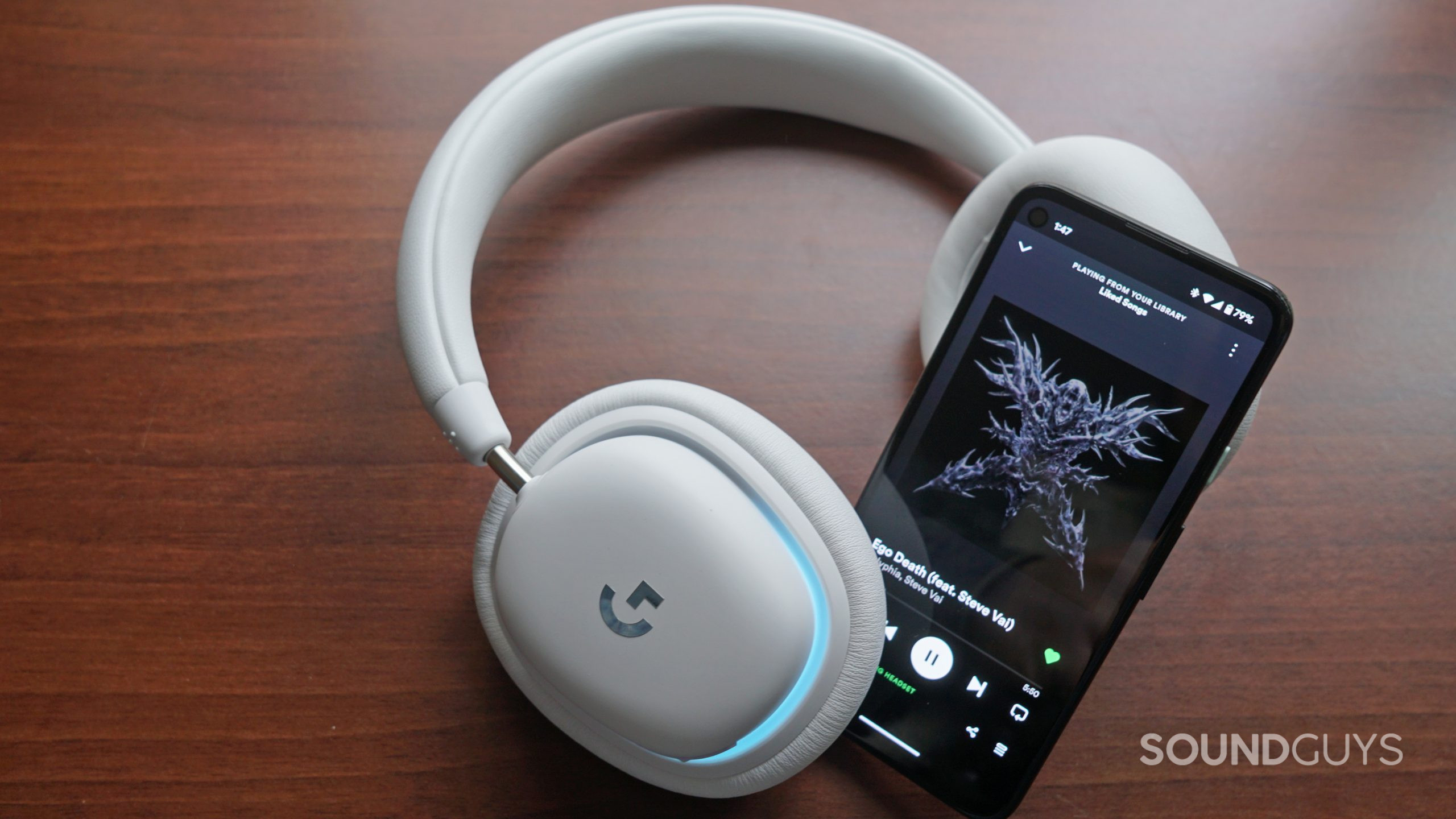 The Logitech G735 lays on a wooden surface next to a Google Pixel 4a.