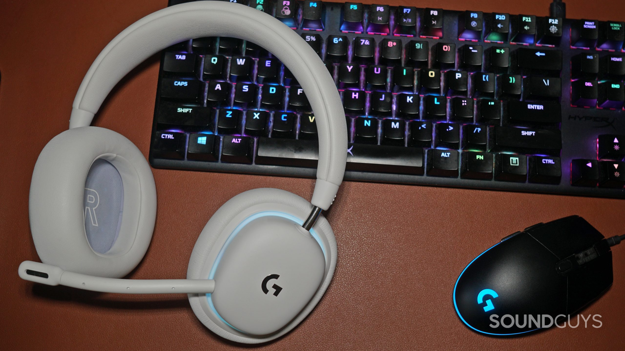 The Logitech G735 gaming headset lays on a leather surface next to a Logitech gaming mouse and a HyperX gaming keyboard.