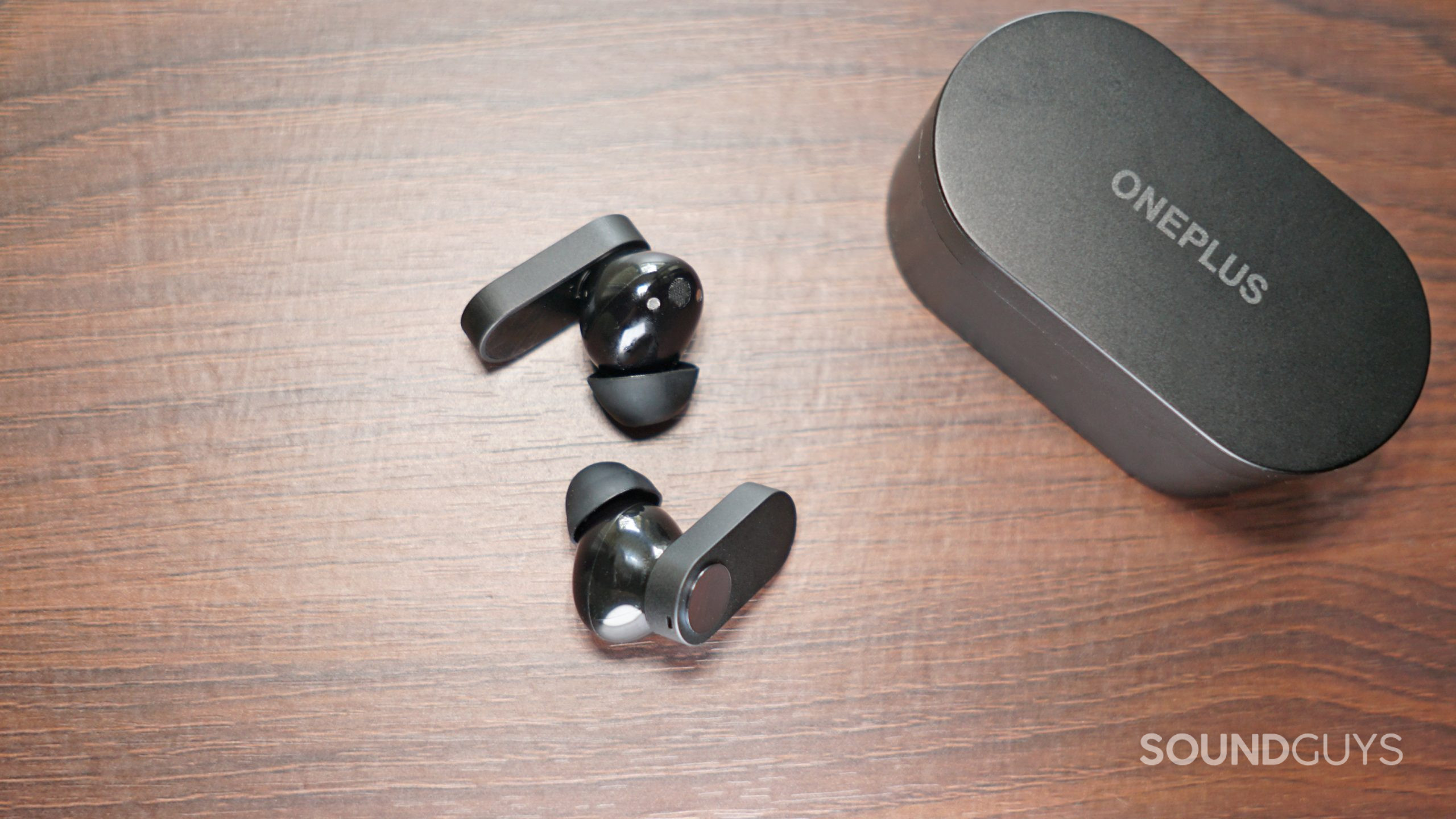 The OnePlus Nord Buds true wireless earbuds lay on a wooden surface.